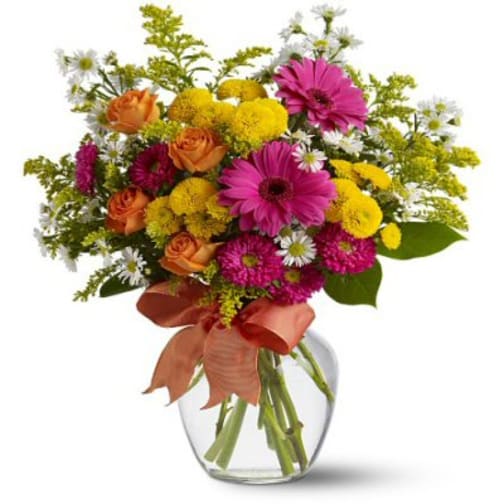 Mixed bouquet of pink, yellow, orange, and white flowers in a clear glass vase
