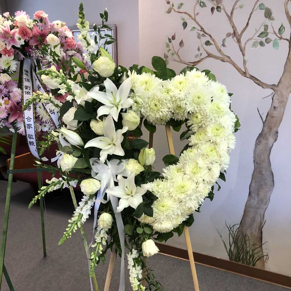 White floral funeral wreath on a wooden stand with ribbon.
