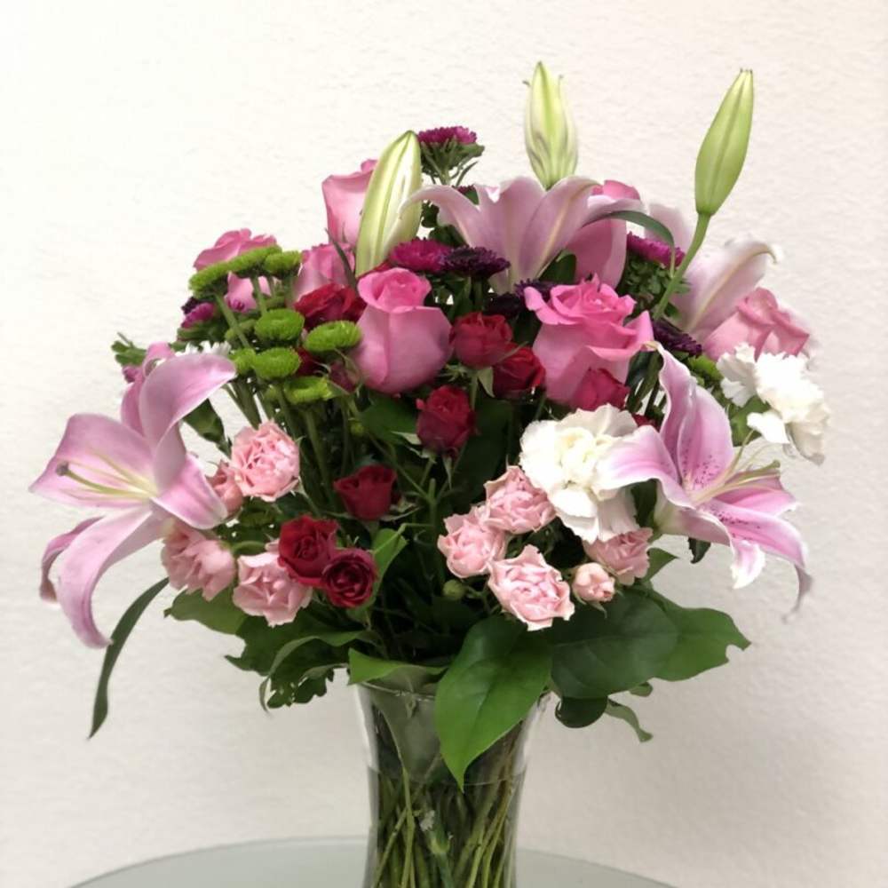 Pink lilies and roses arranged in a clear glass vase