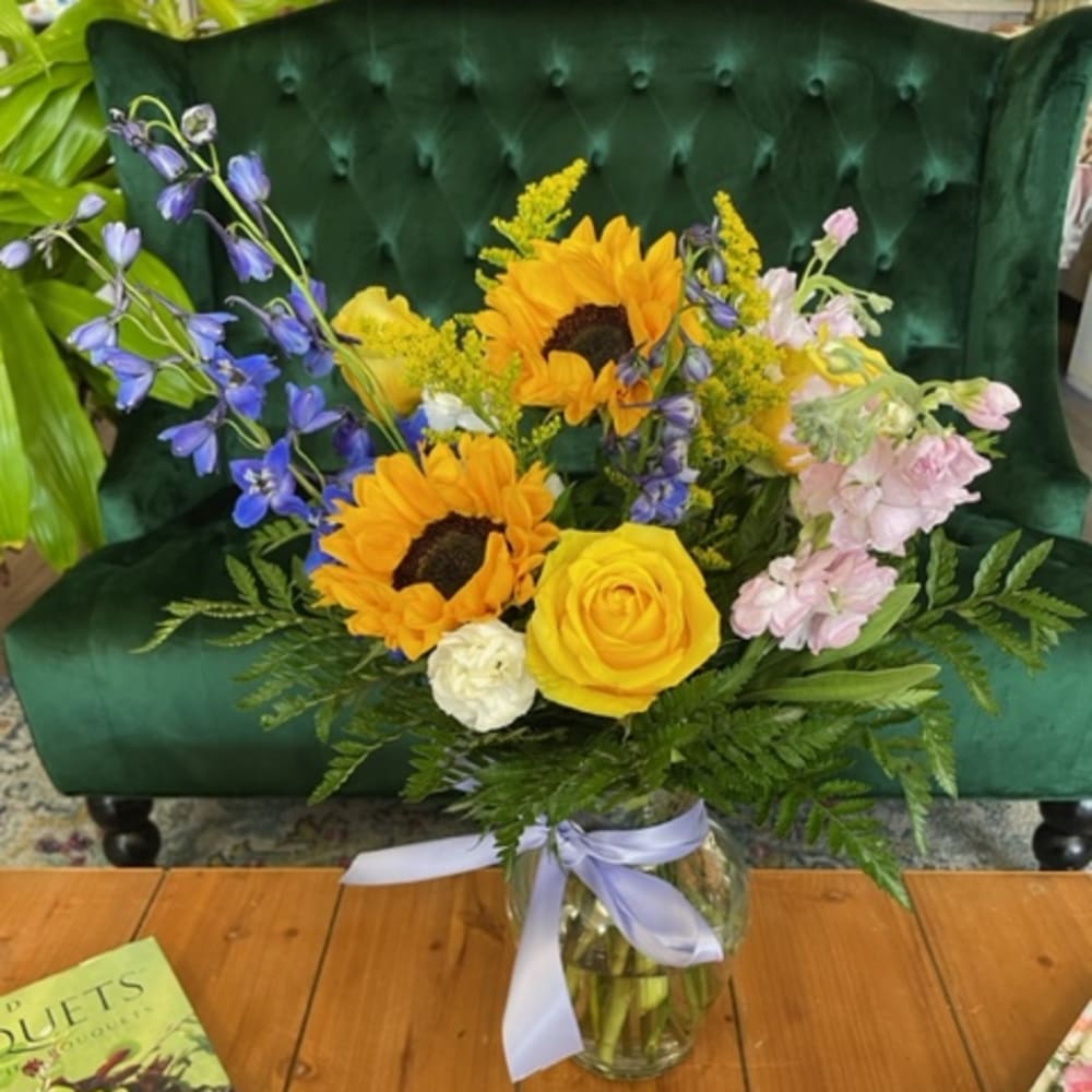 Bouquet of sunflowers, yellow roses, and blue flowers in a glass vase