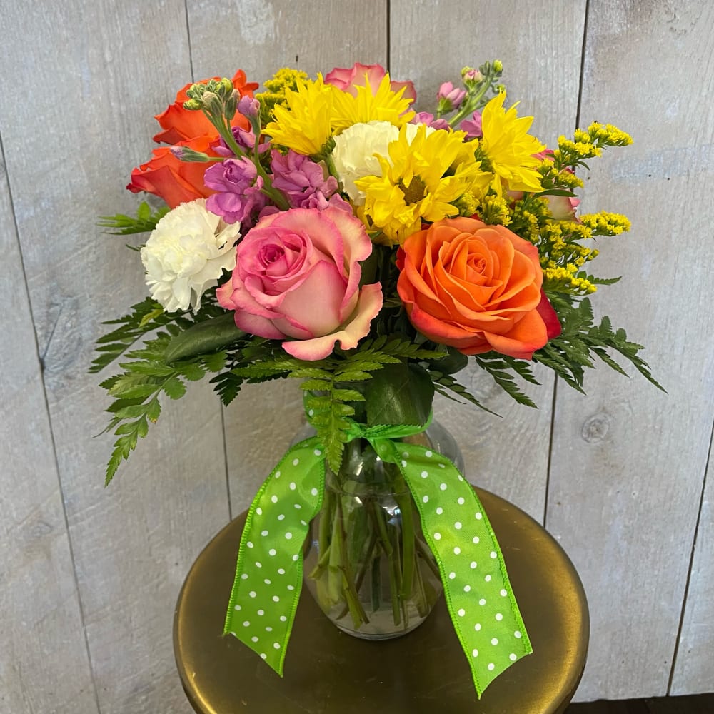 Mixed bouquet of roses, daisies, and carnations in a glass vase with a green ribbon