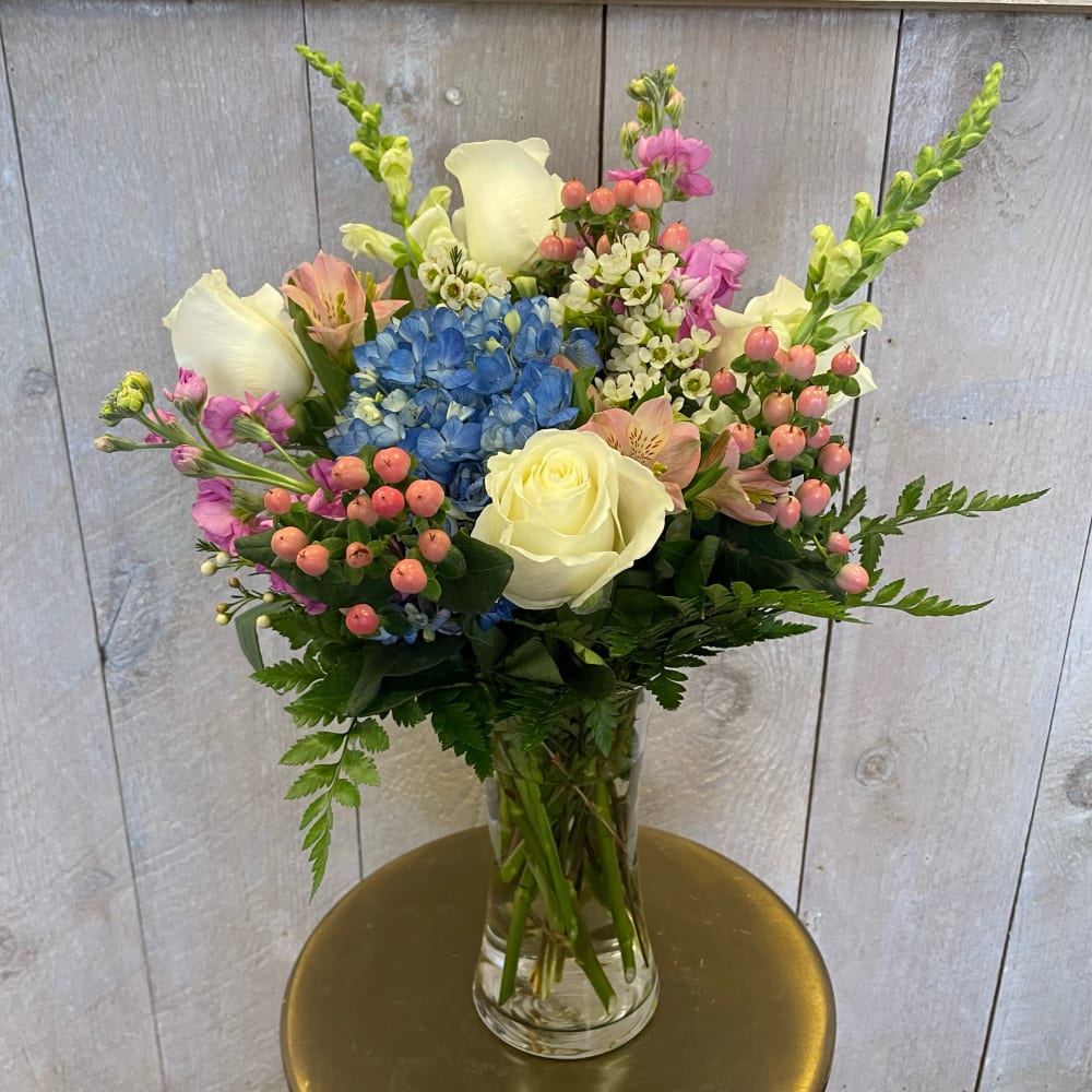 Mixed bouquet with white roses, blue hydrangea, and pink flowers in a glass vase