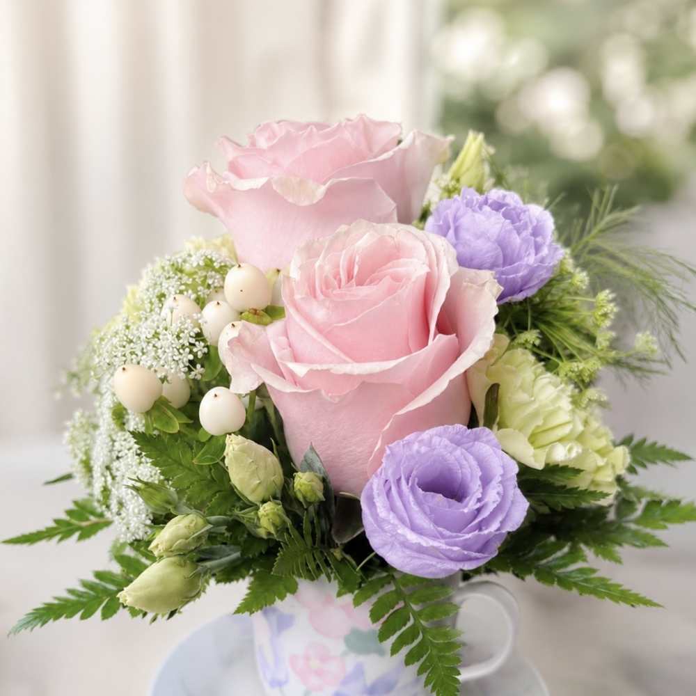 Pink and lavender roses arranged in a teacup with a saucer