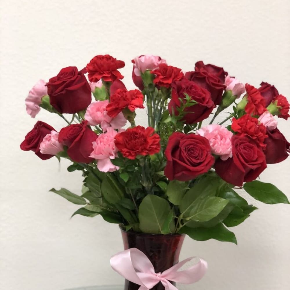 Red roses and pink carnations in a burgundy vase with a pink ribbon
