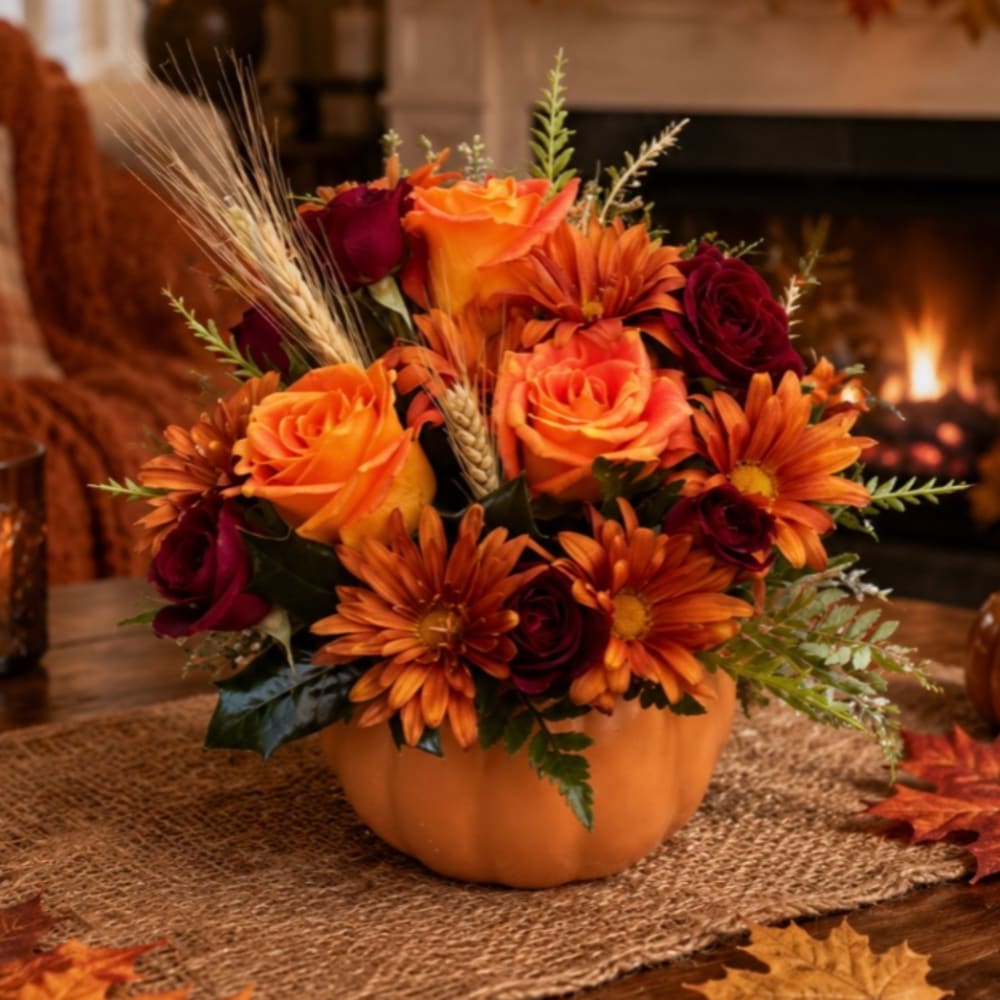 Orange and burgundy flower arrangement in a pumpkin-shaped container