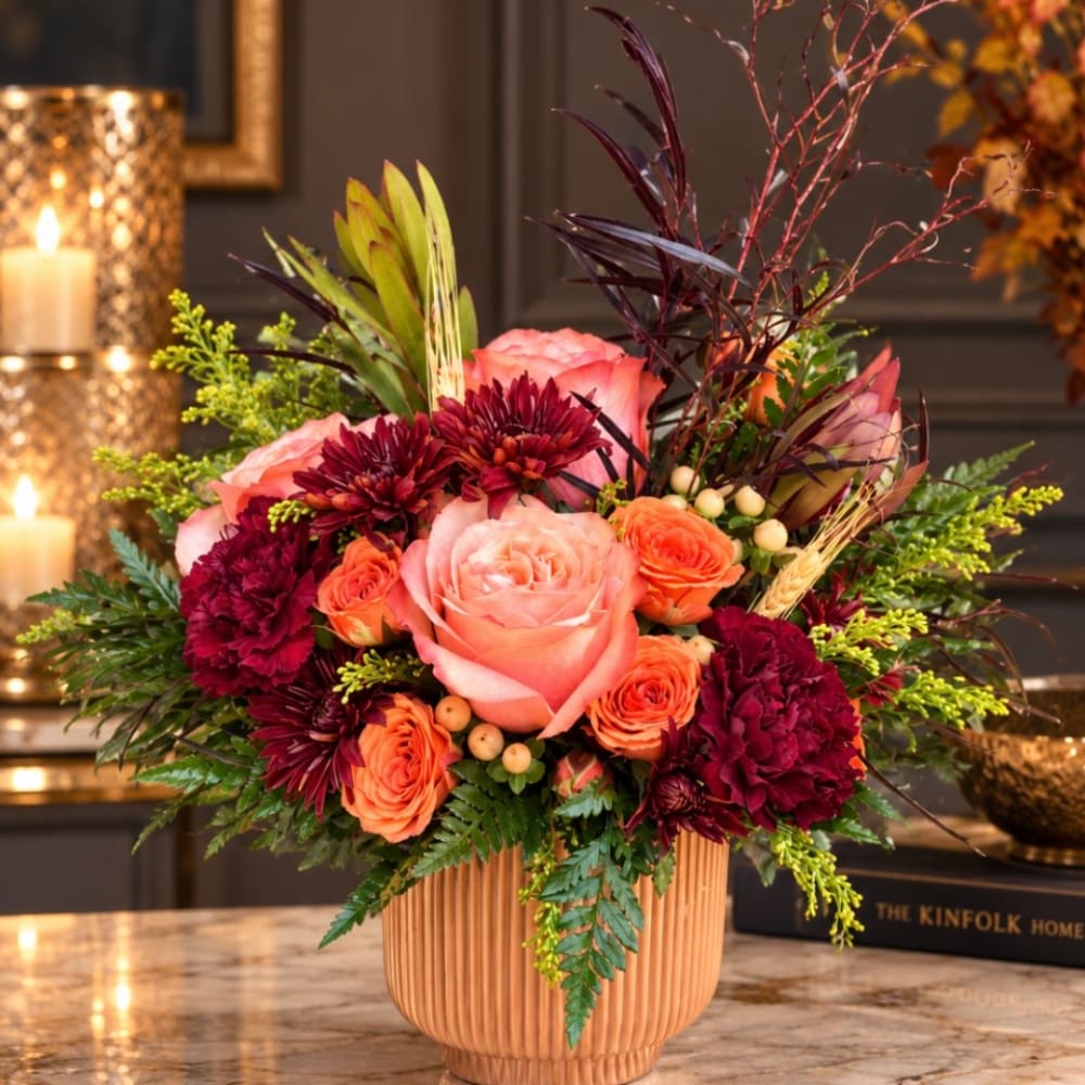 Pink and orange roses with burgundy flowers in a ribbed vase