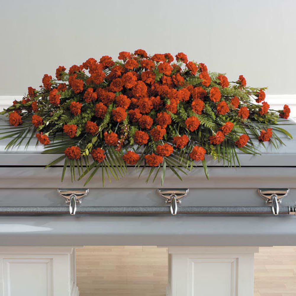 Orange carnation casket spray arranged across a closed light-colored casket