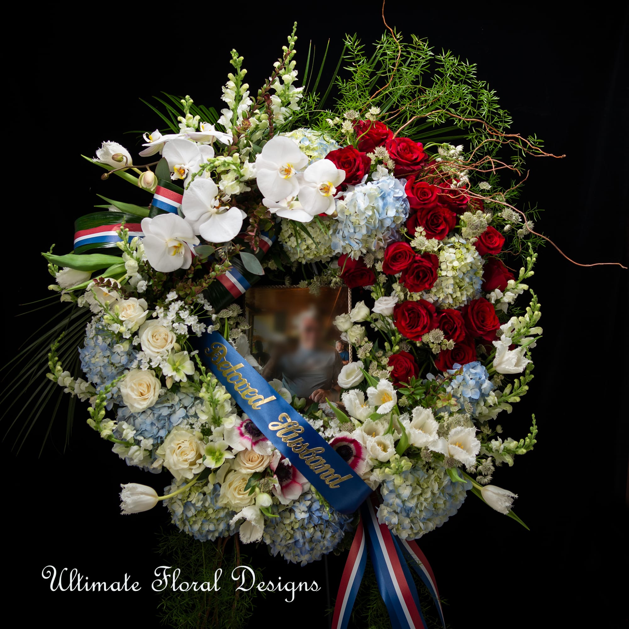 Large funeral wreath with red roses, white orchids, and blue hydrangeas