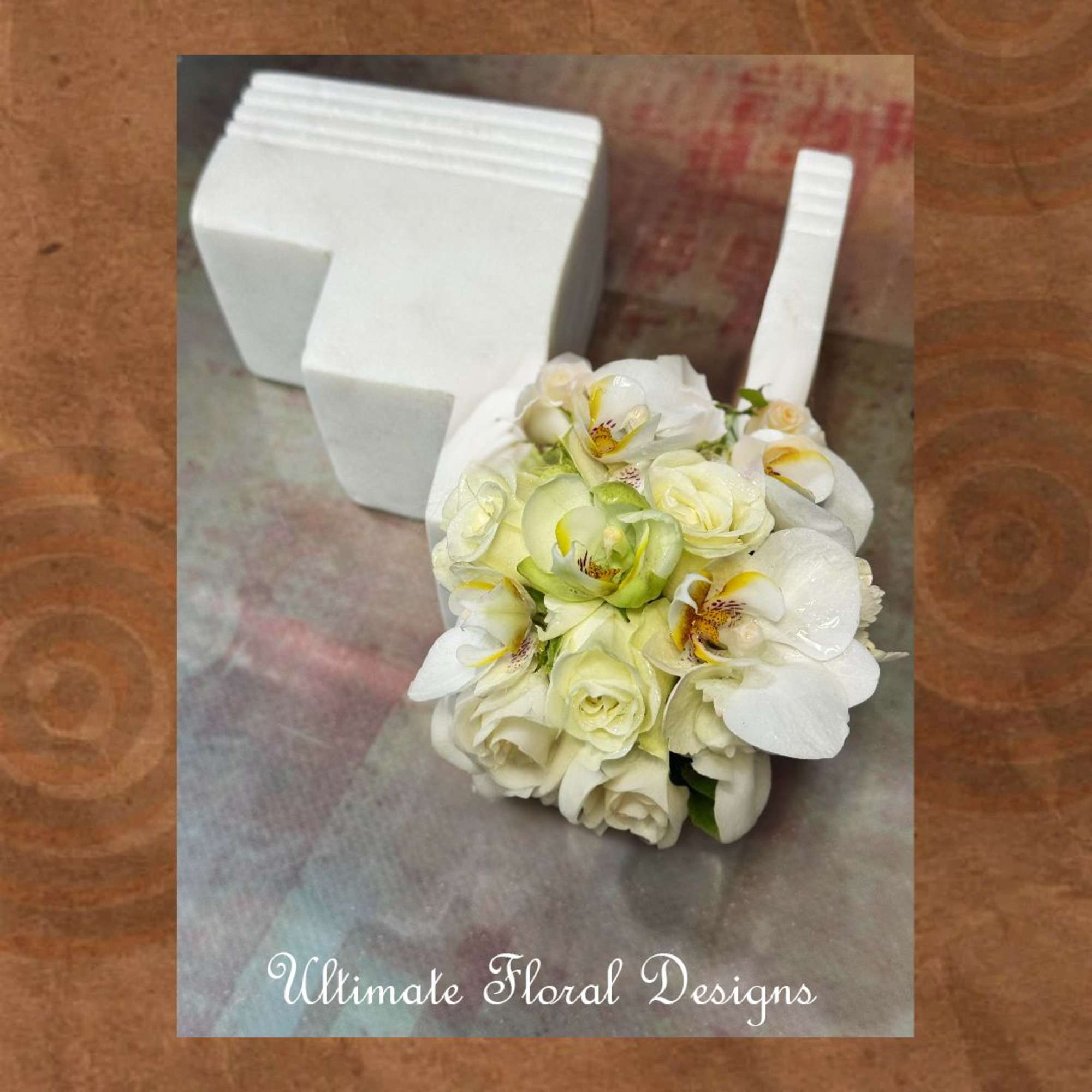 White floral bouquet with orchids and roses beside a white foam holder