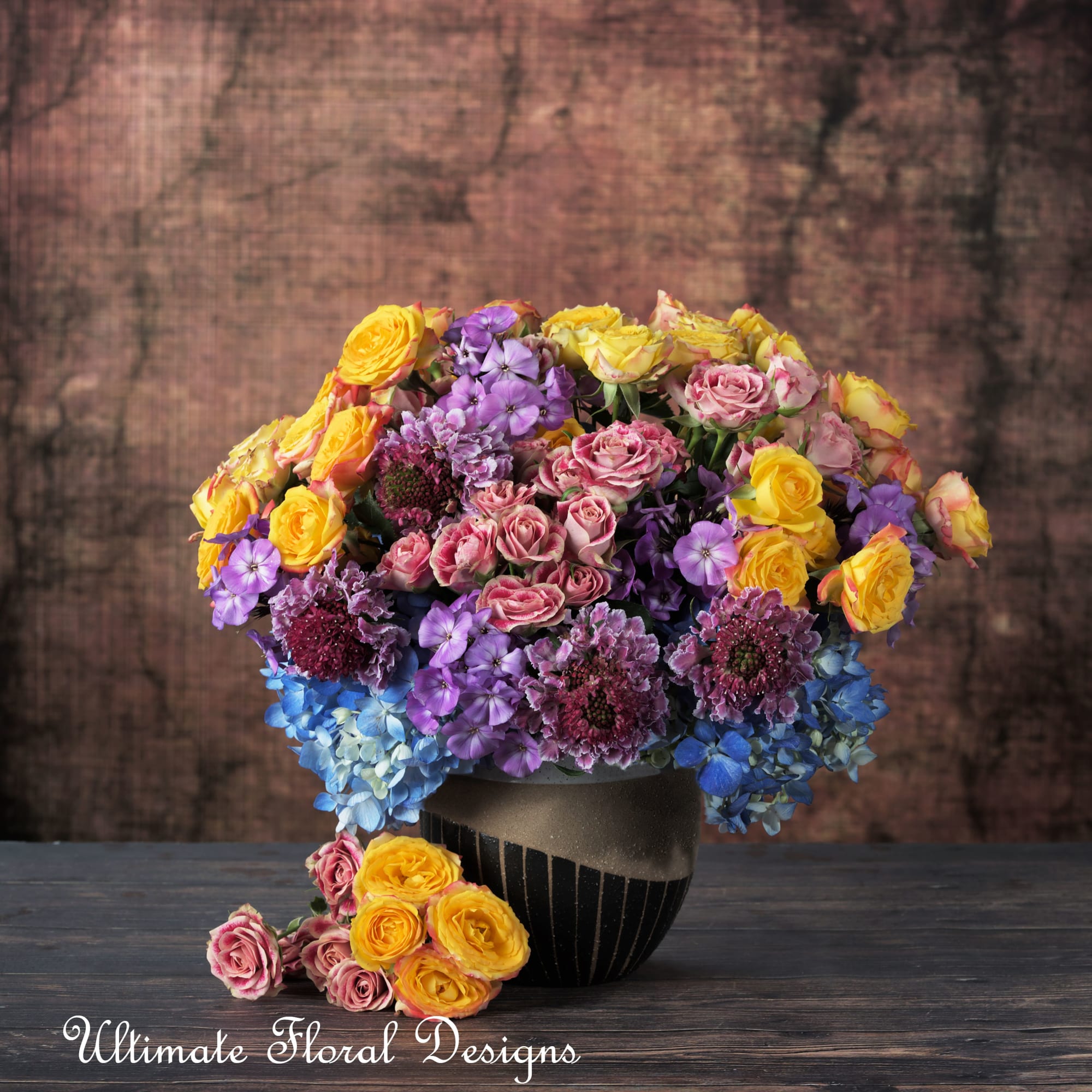 Mixed bouquet of yellow, pink, purple, and blue flowers in a dark vase
