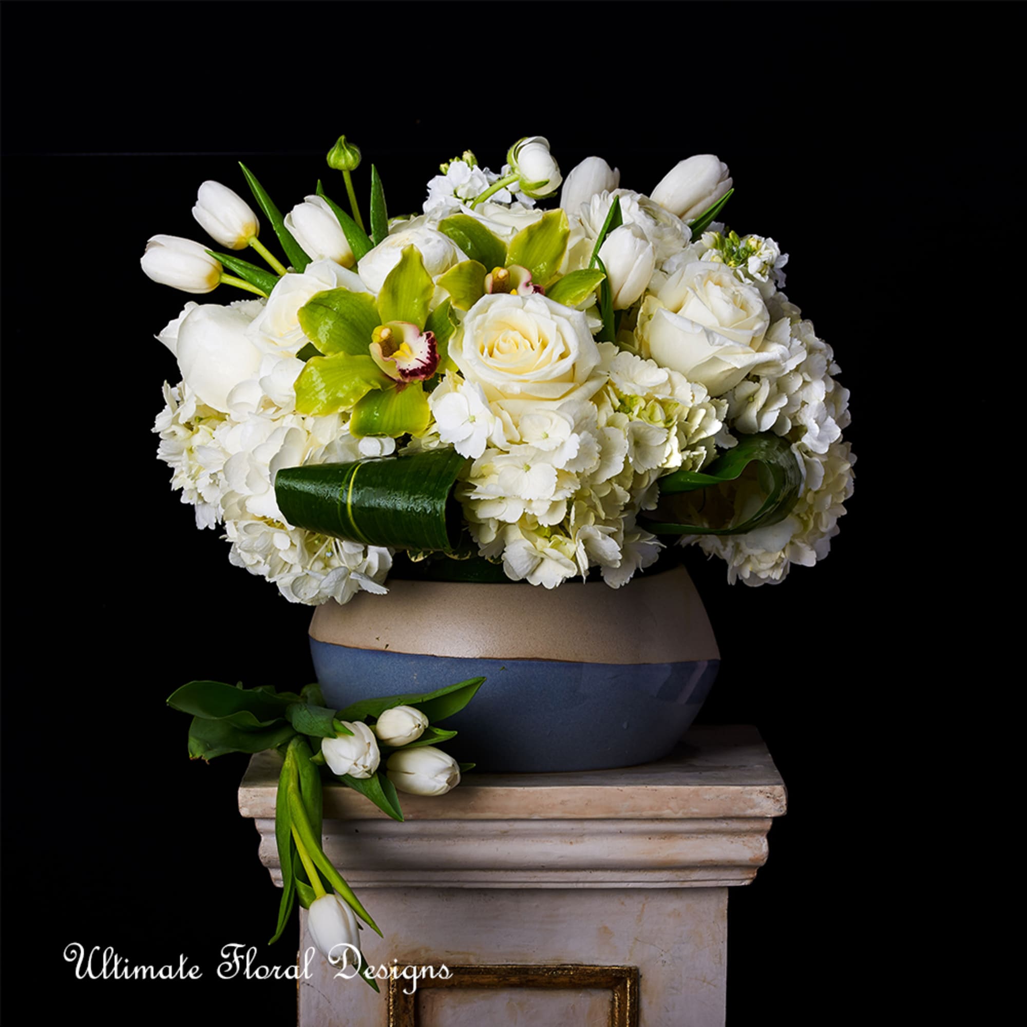 White roses and tulips arranged in a low vase with green orchids