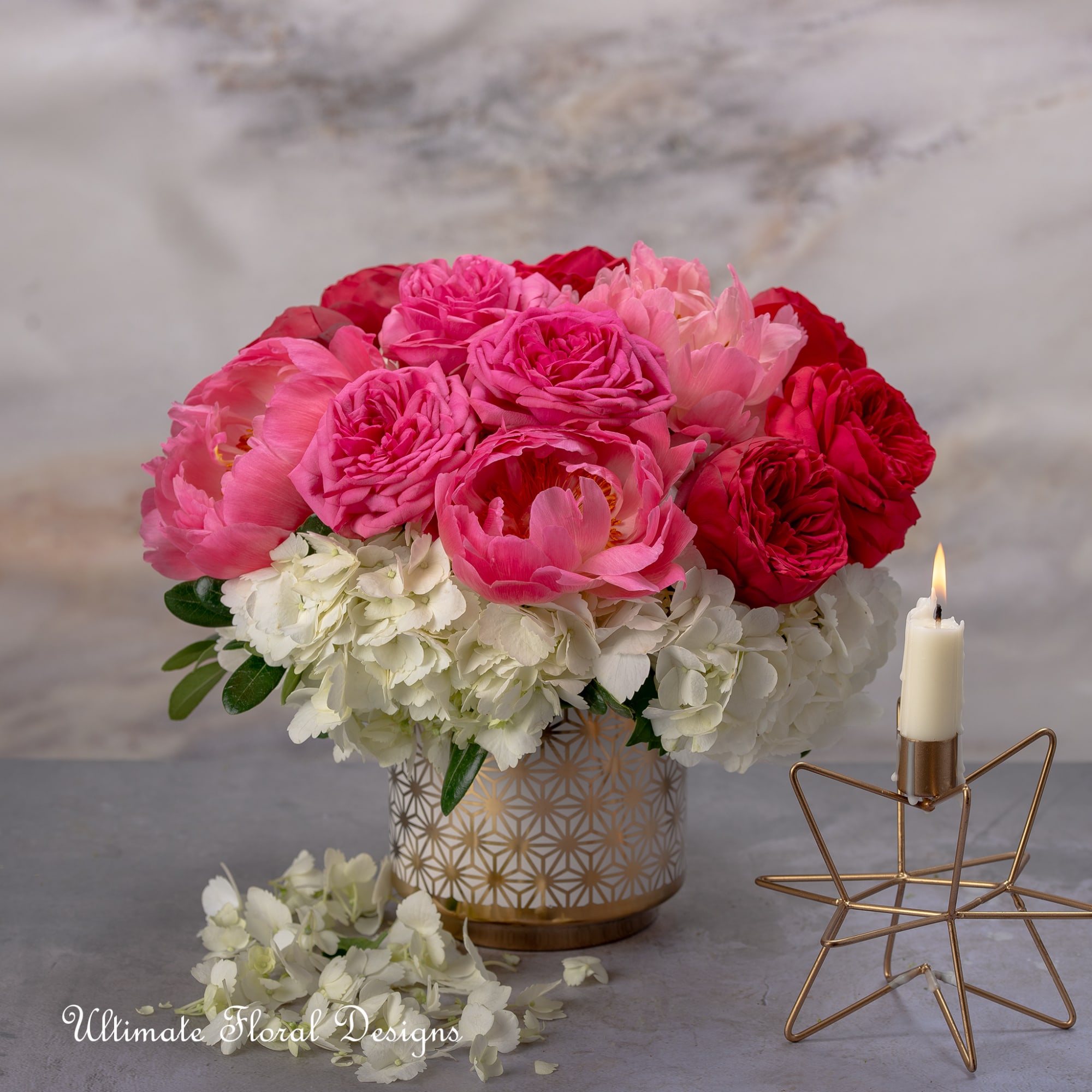 Pink and red flower arrangement in a patterned vase beside a lit candle.