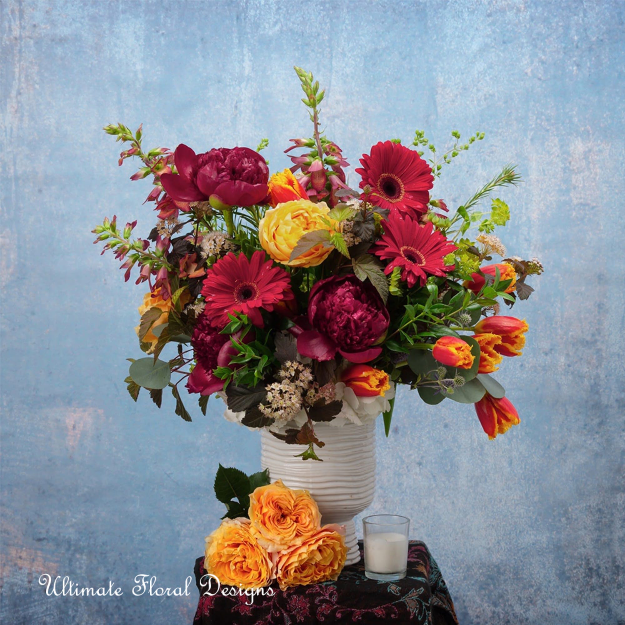 Colorful mixed flower arrangement in a white vase with orange roses below