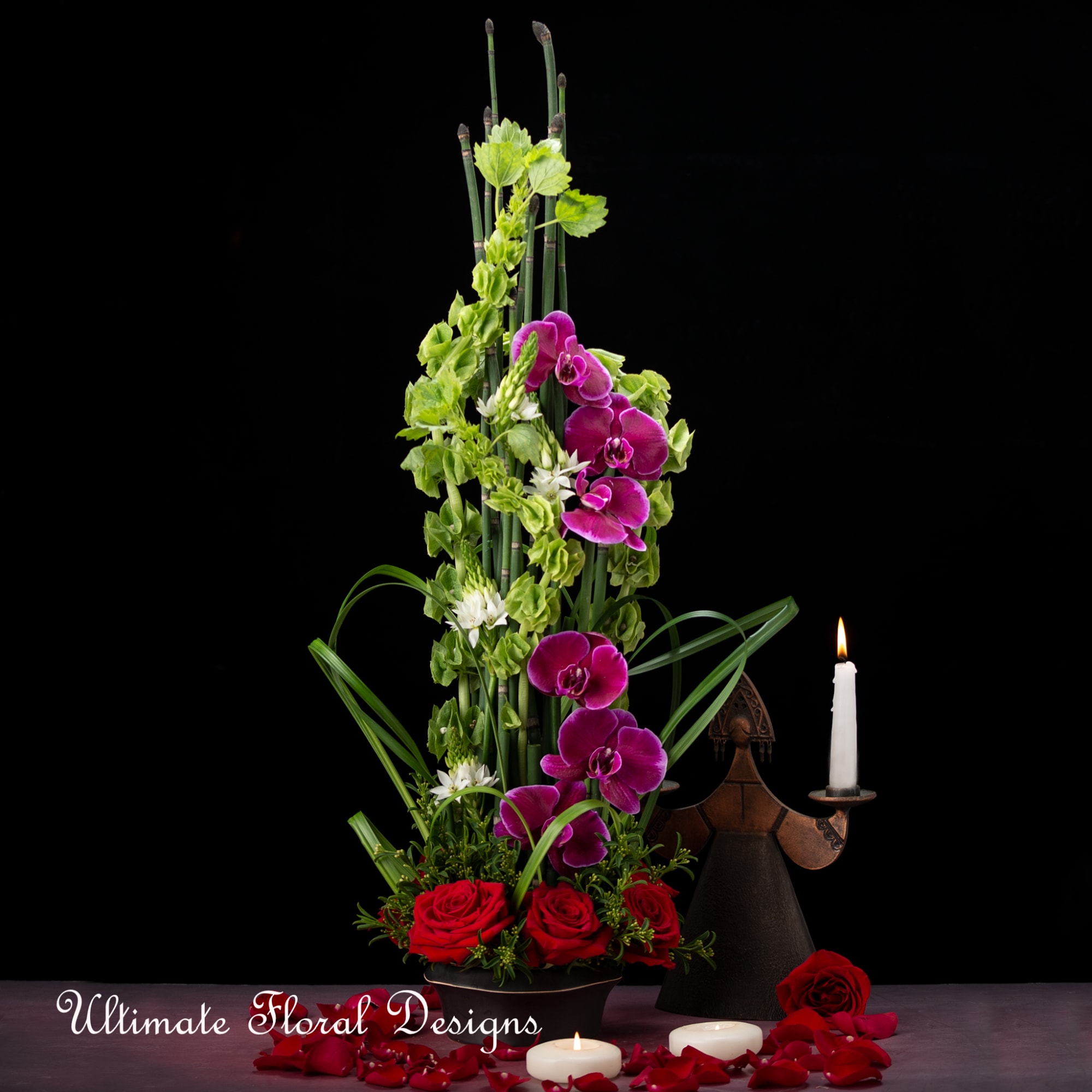 Tall floral arrangement with purple orchids, red roses, and candles