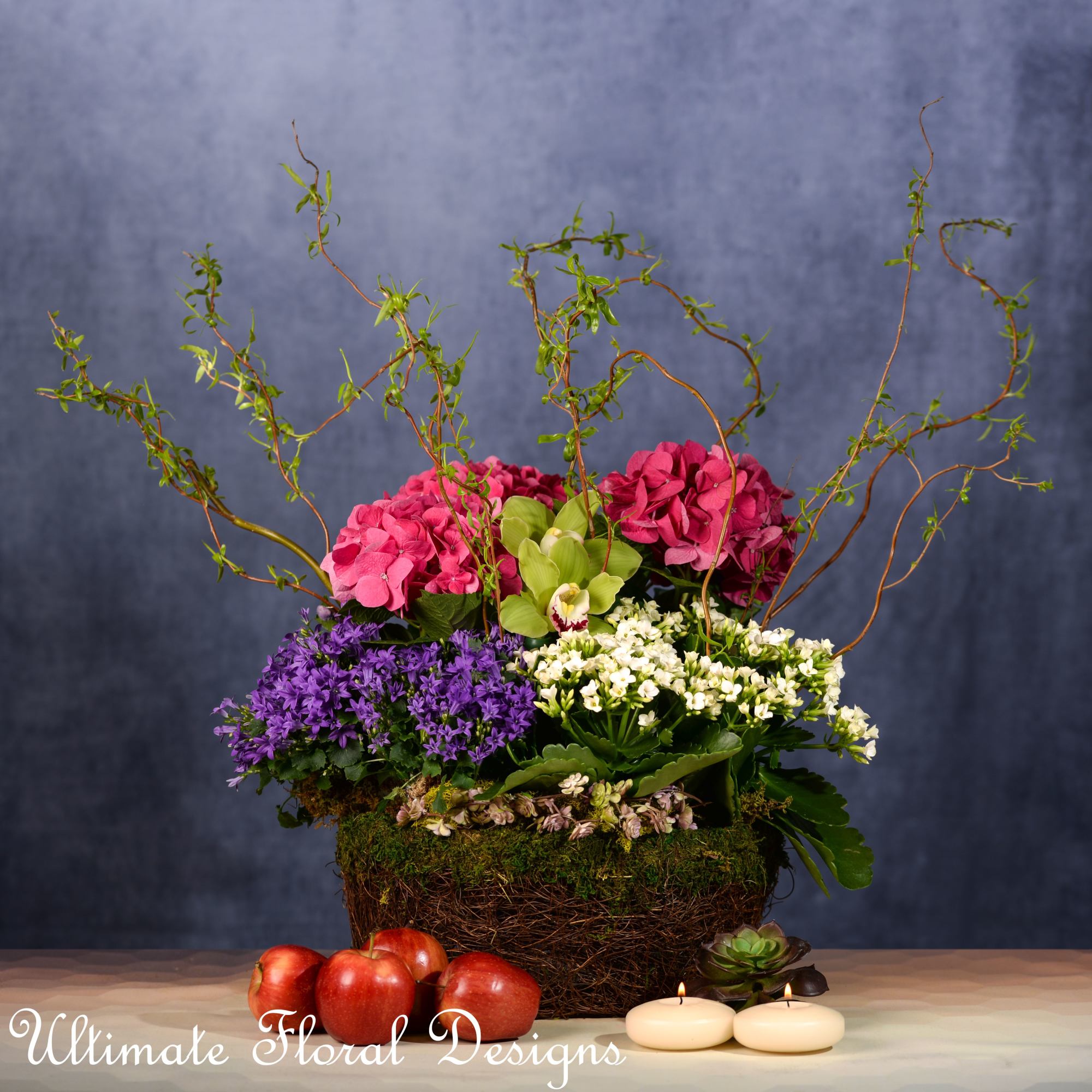 Colorful floral arrangement in a woven basket with apples and candles