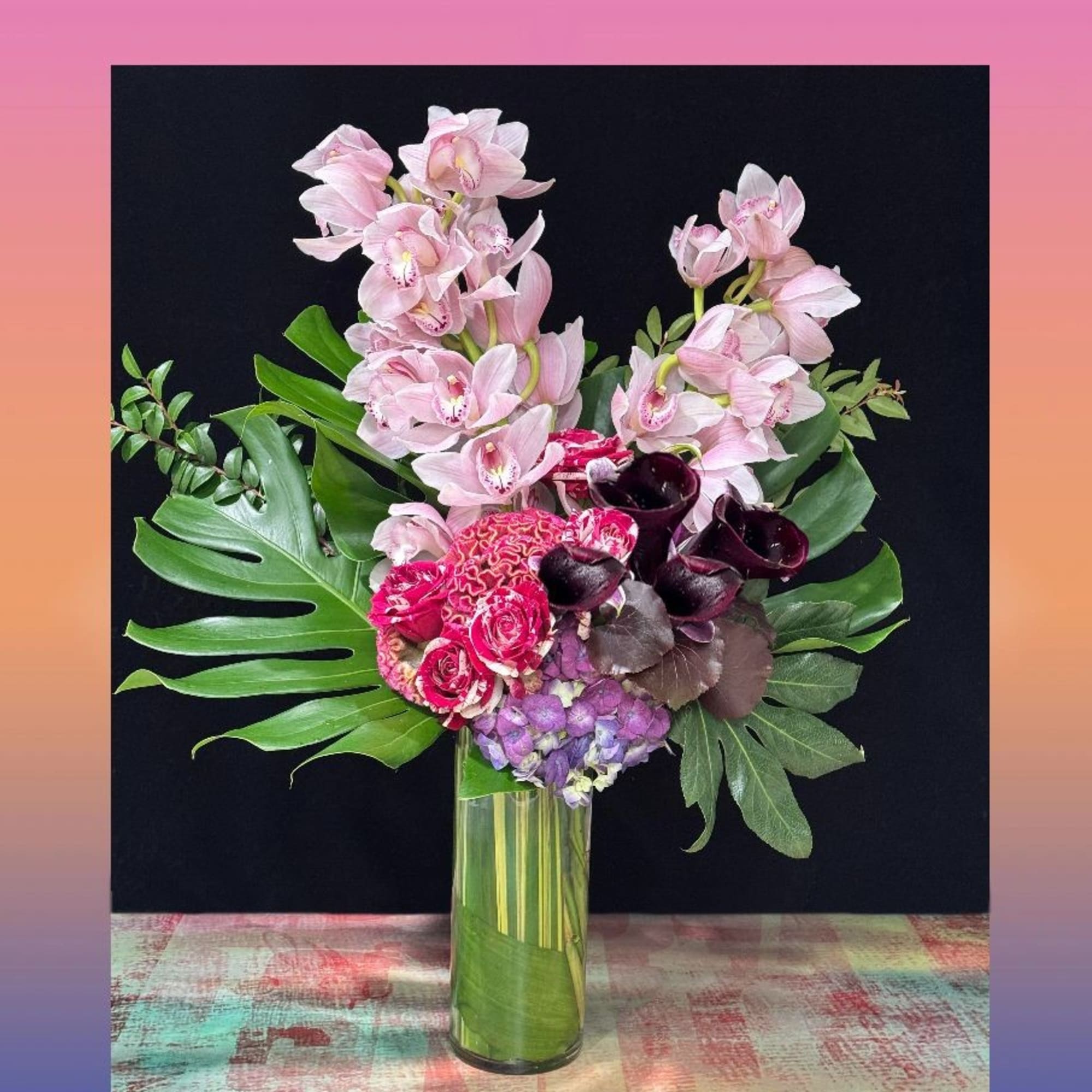 Pink orchids and mixed flowers arranged in a tall glass vase