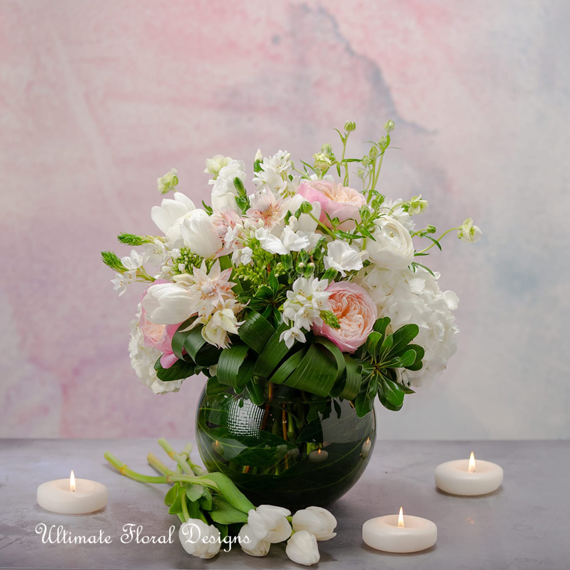 Pink and white floral arrangement in a round glass vase with candles