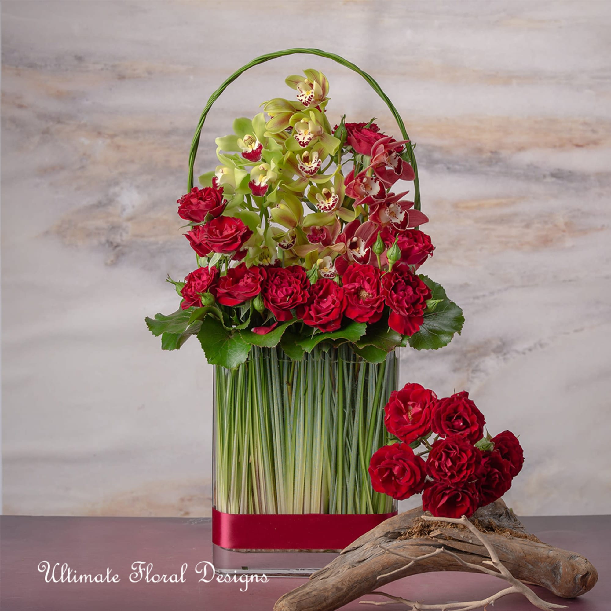 Red roses and green orchids in a tall glass vase with a curved handle