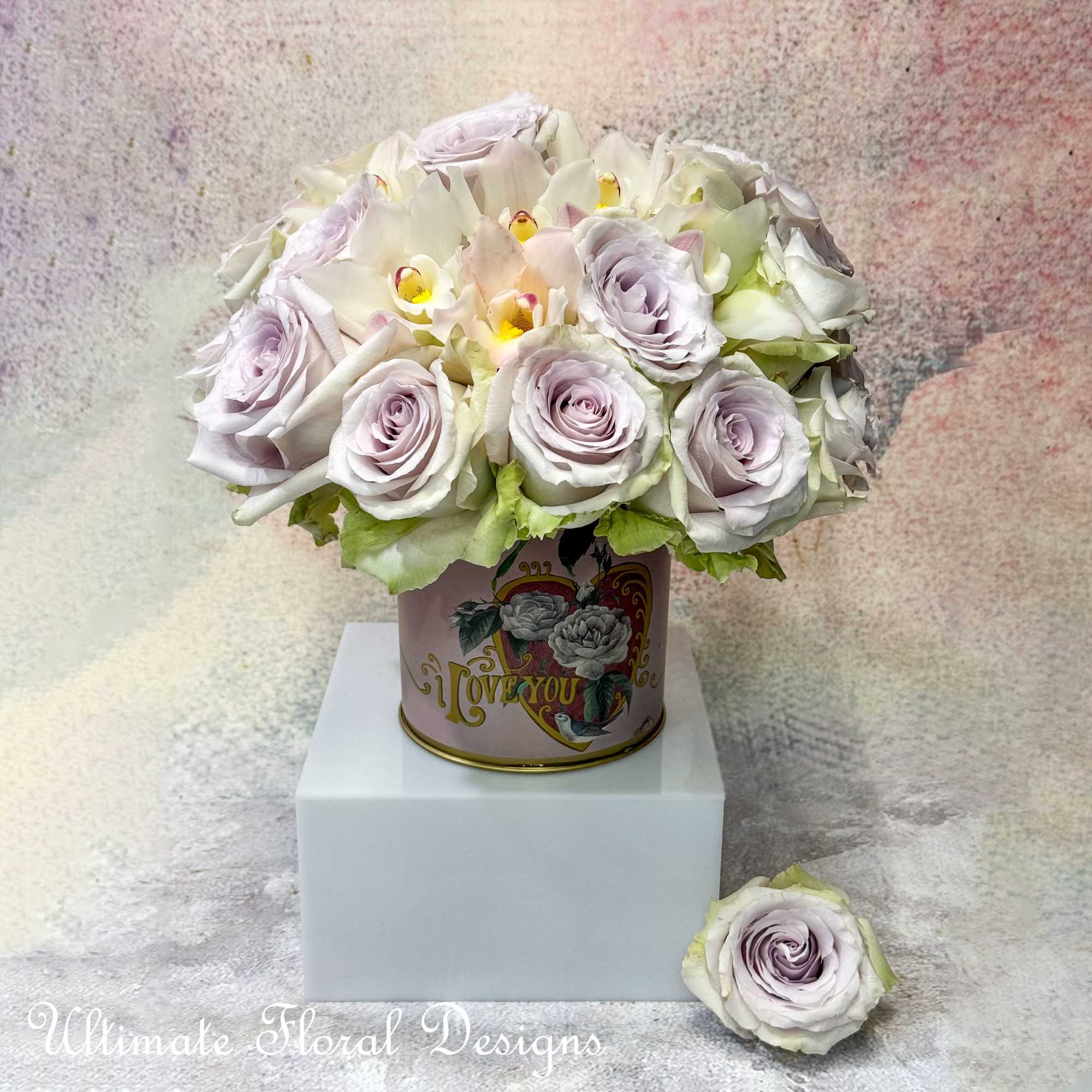 Lavender roses and white orchids arranged in a decorative tin box