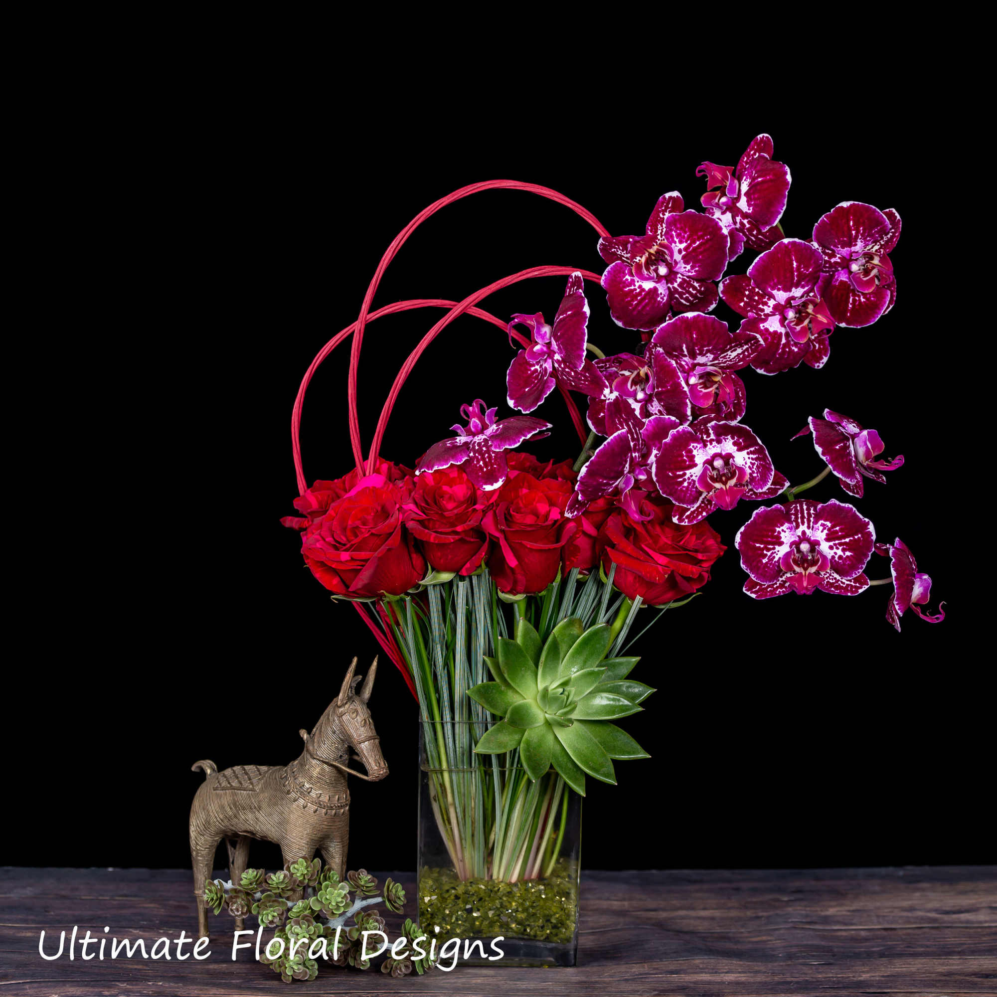 Red roses and magenta orchids in a glass vase with a small horse figurine