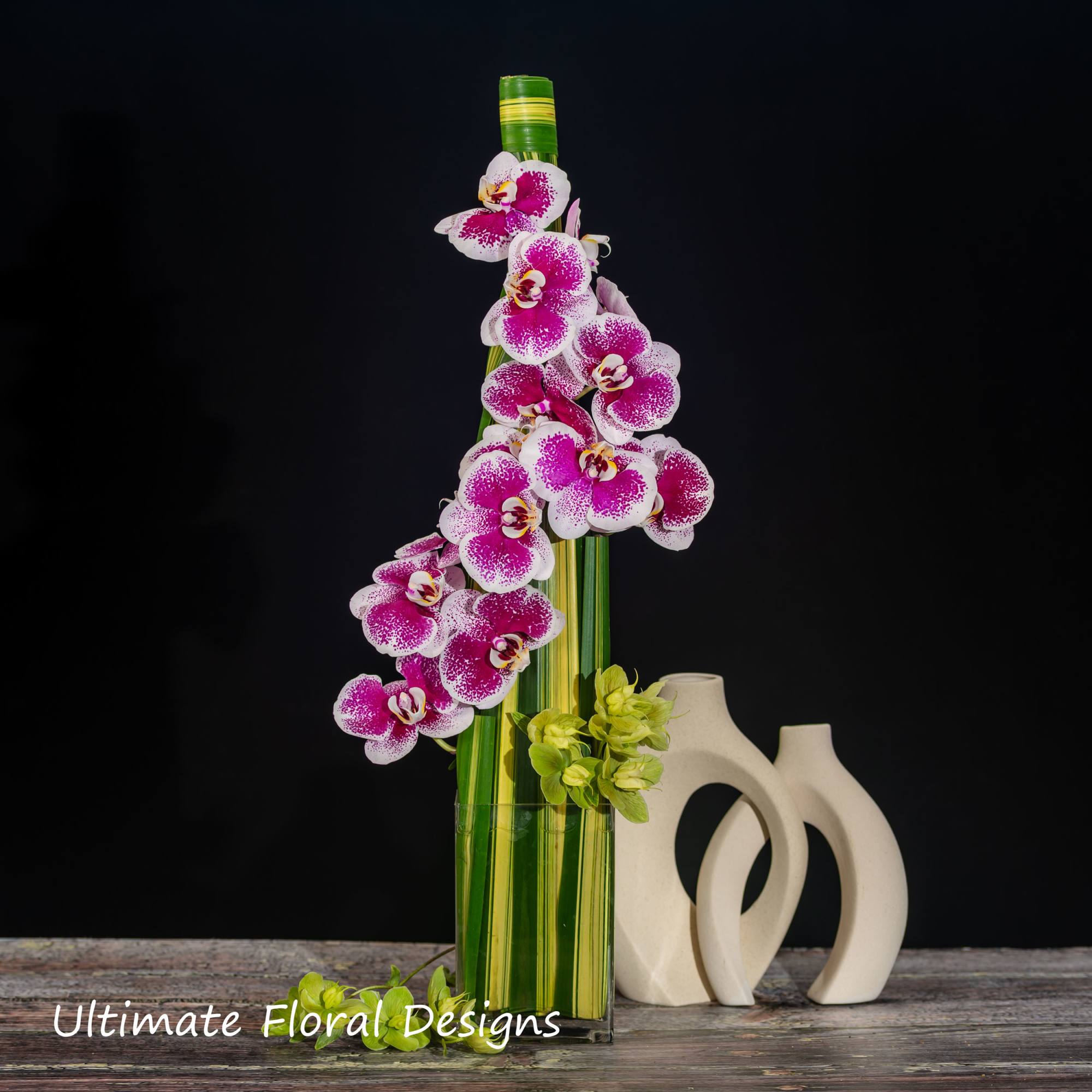 Pink and white orchids in a tall glass vase with green accents