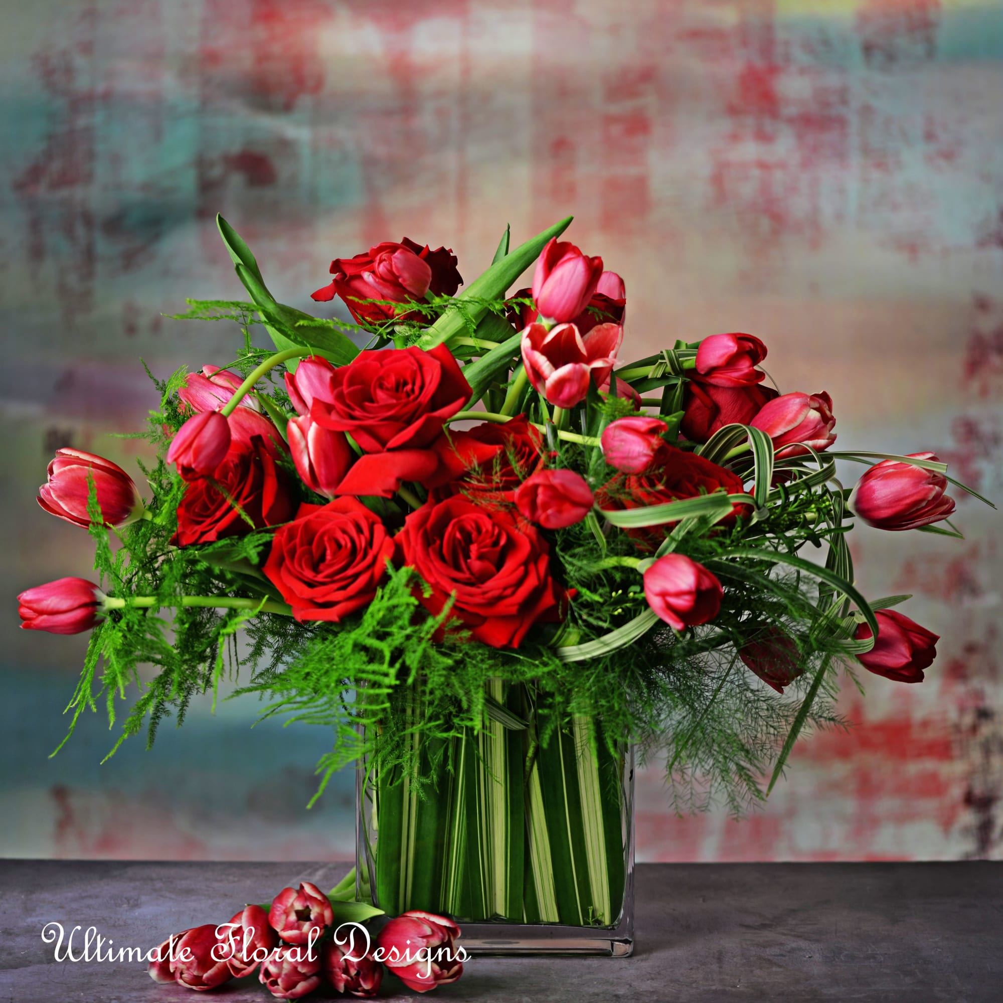 Red roses and pink tulips arranged in a clear square vase