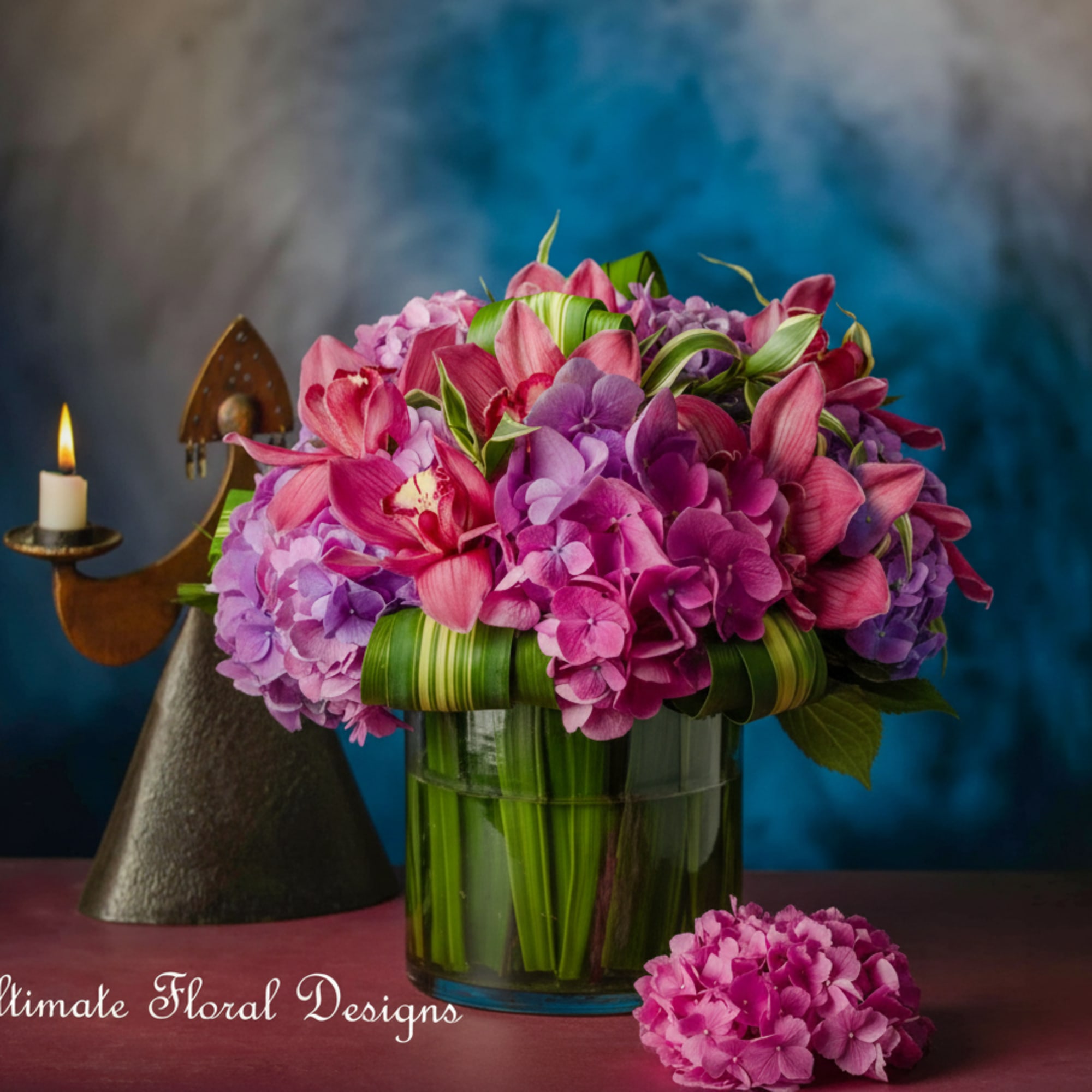 Pink and purple floral arrangement in a glass vase with a candle holder beside it