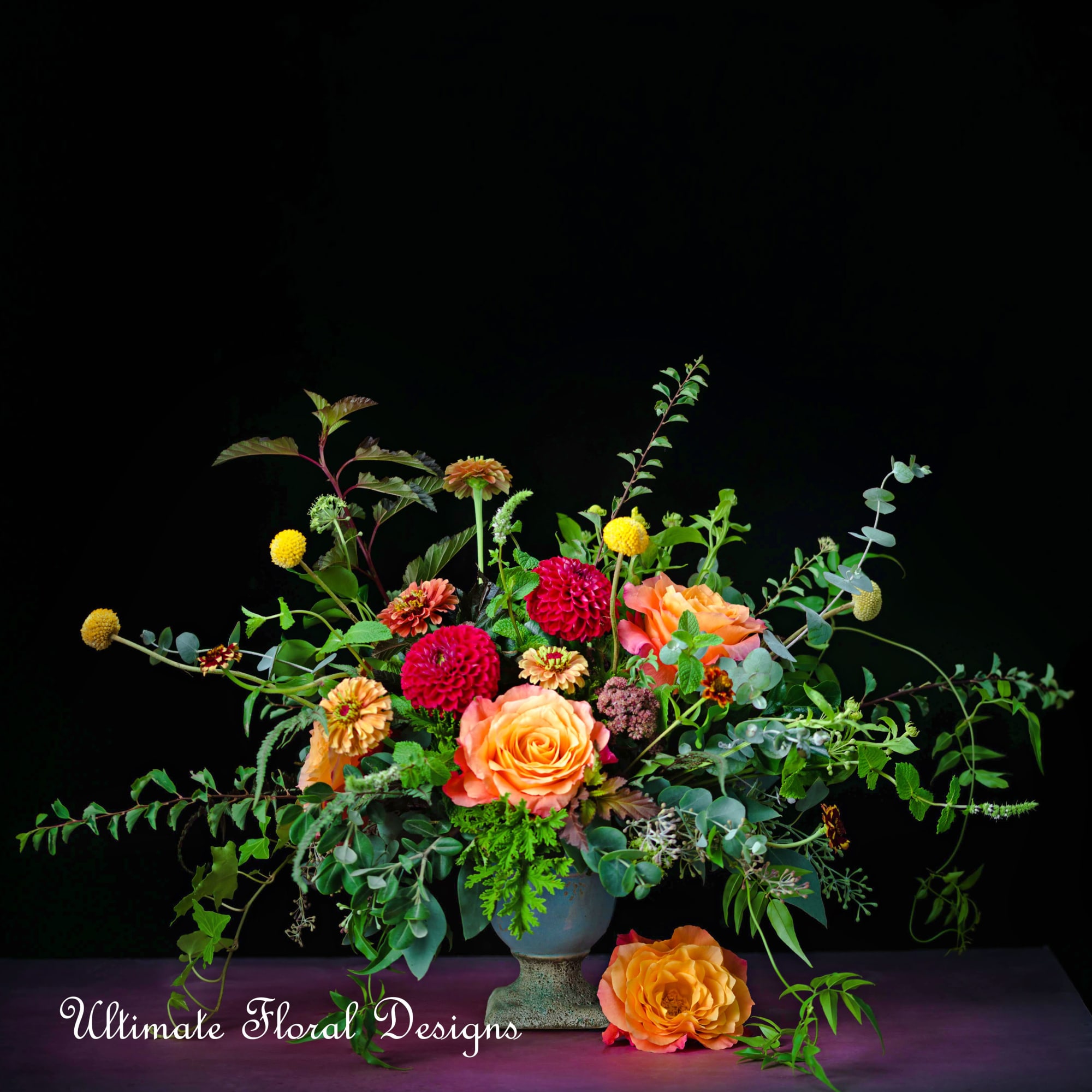 Orange and pink floral arrangement in a blue vase with trailing greenery