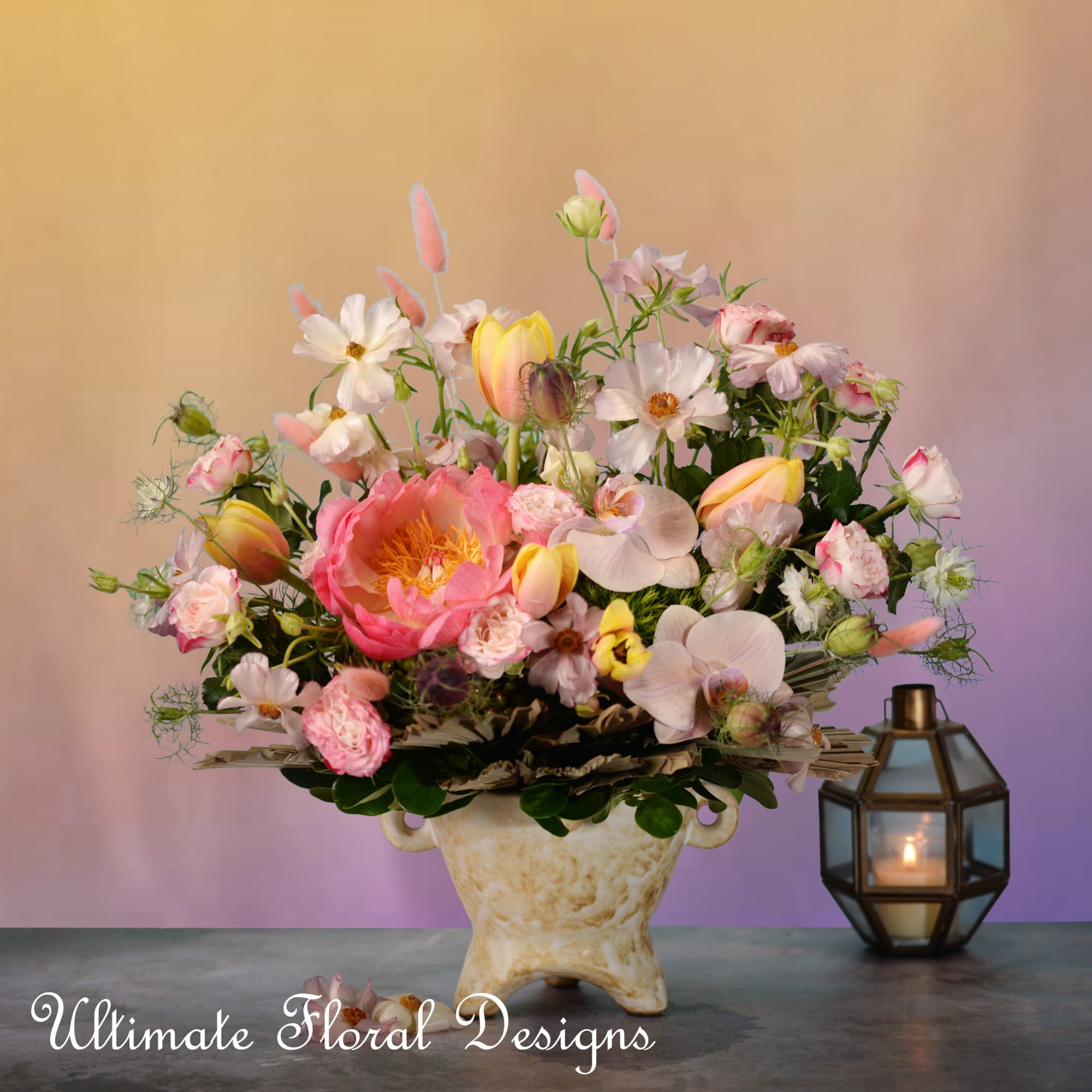 Pink and white mixed flower arrangement in a cream vase beside a lantern