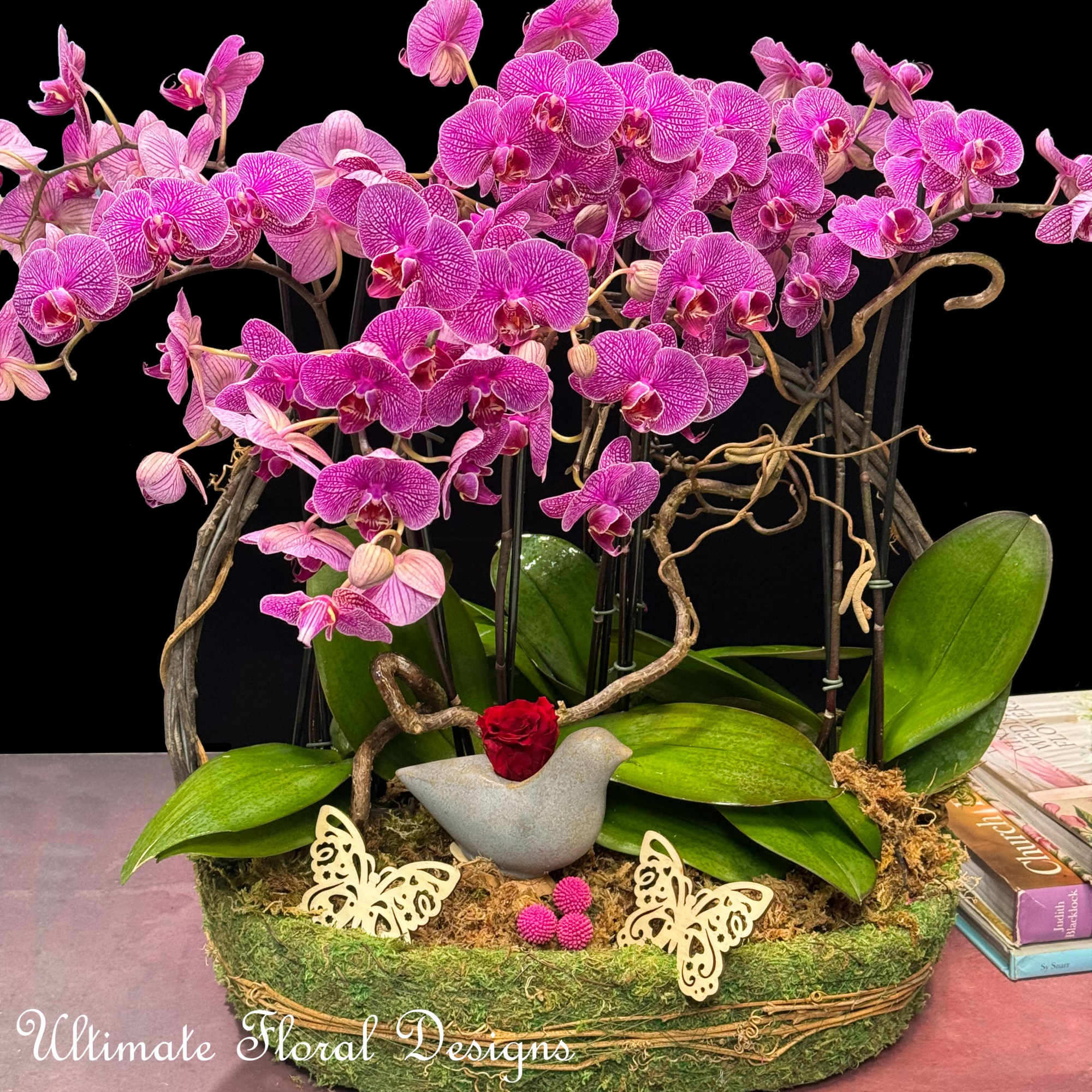Pink orchids arranged in a moss-covered basket with a small red rose accent