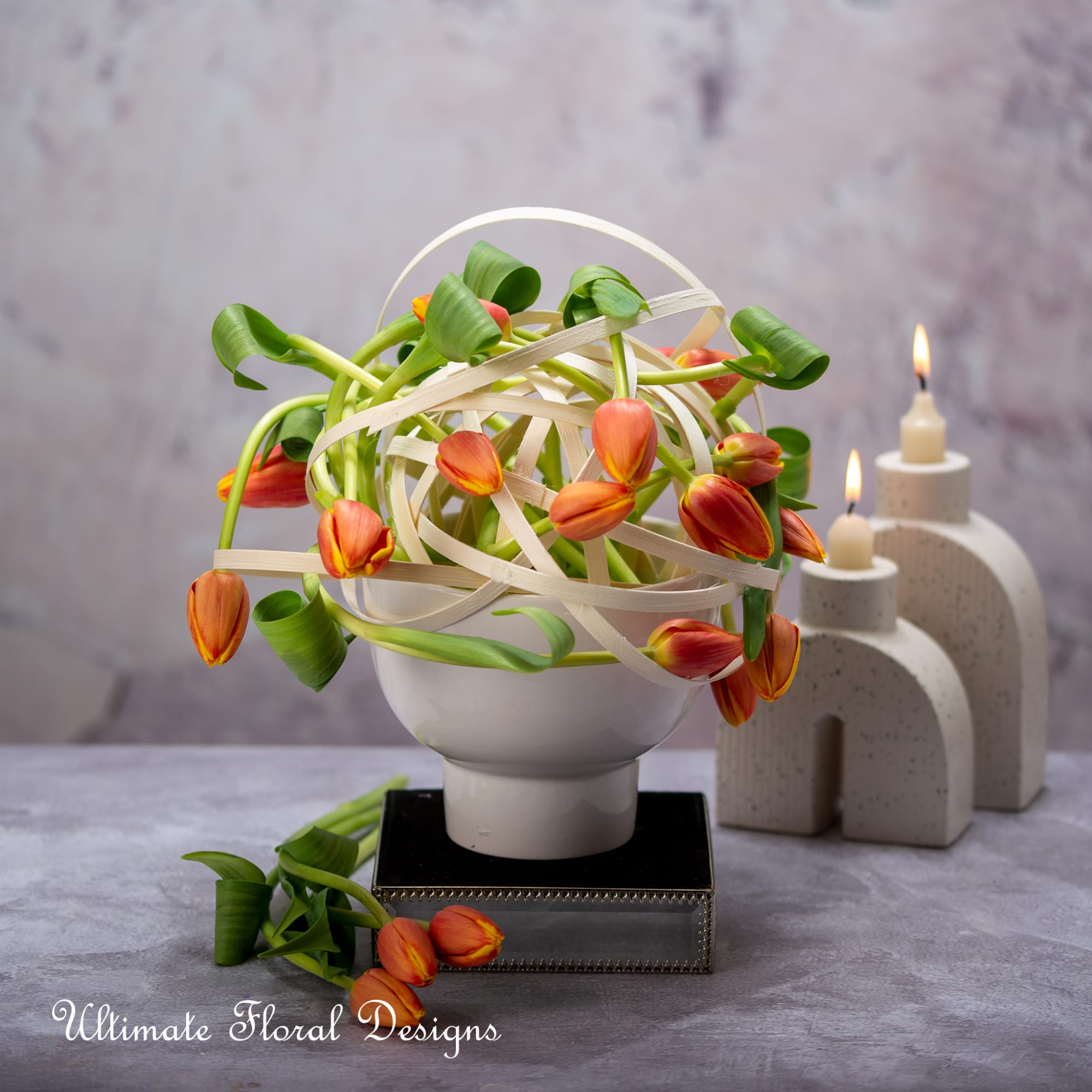 Orange tulips arranged in a white vase with looping ribbon accents