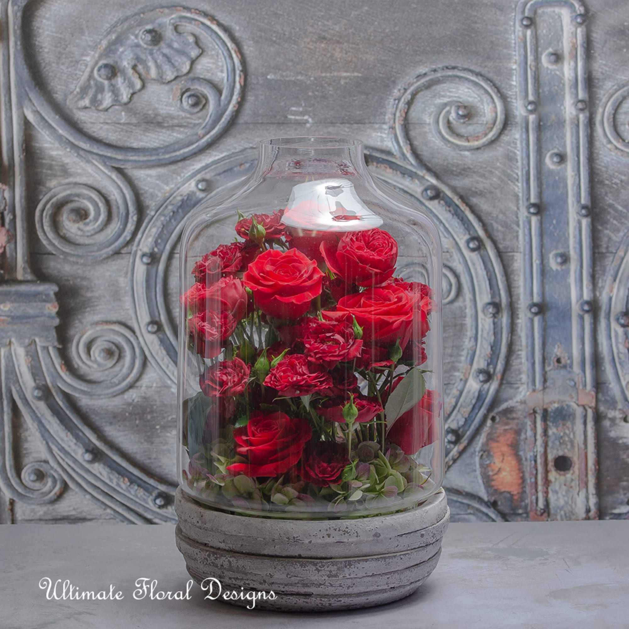 Red roses and carnations under a glass cloche on a gray base