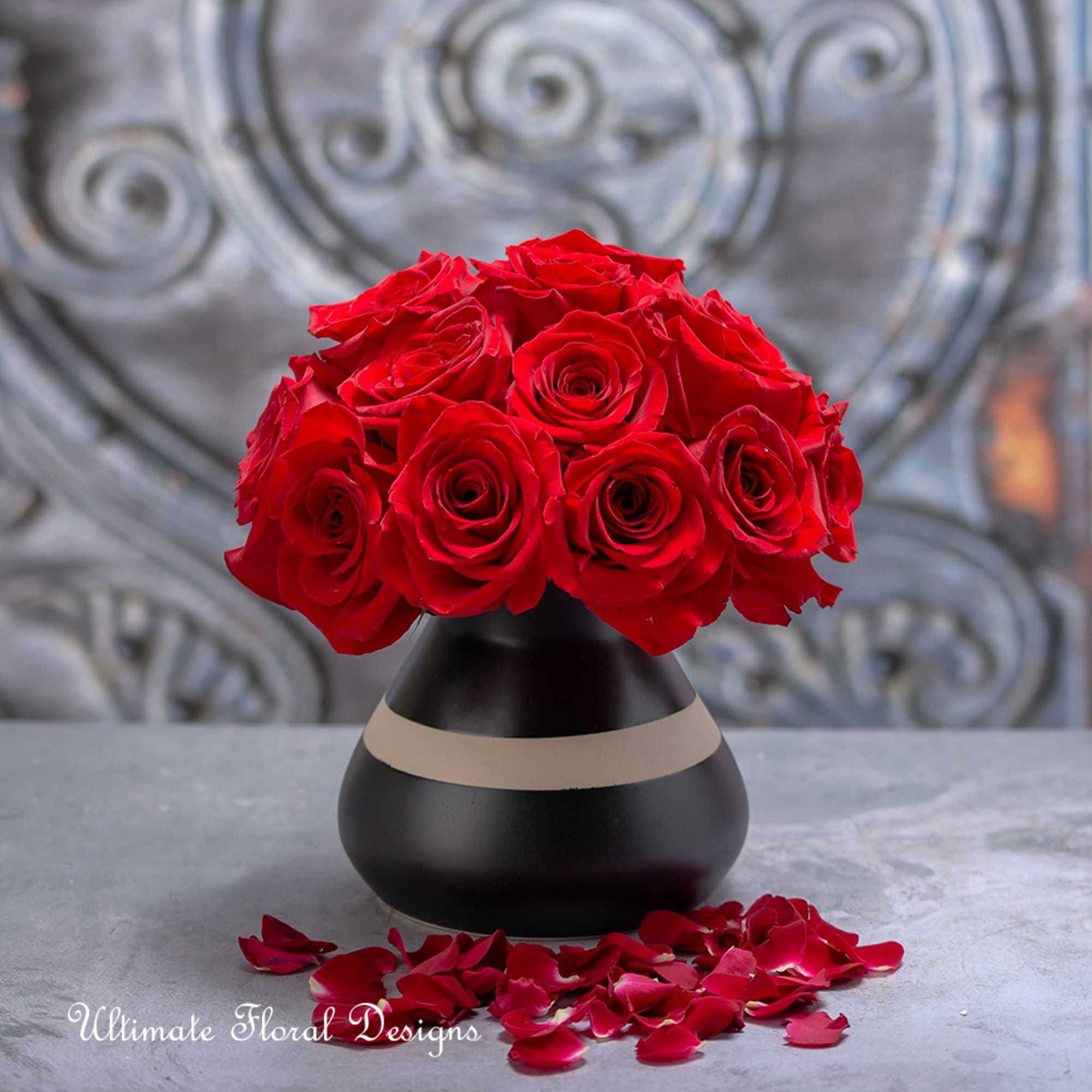 Red rose bouquet in a black vase with scattered petals