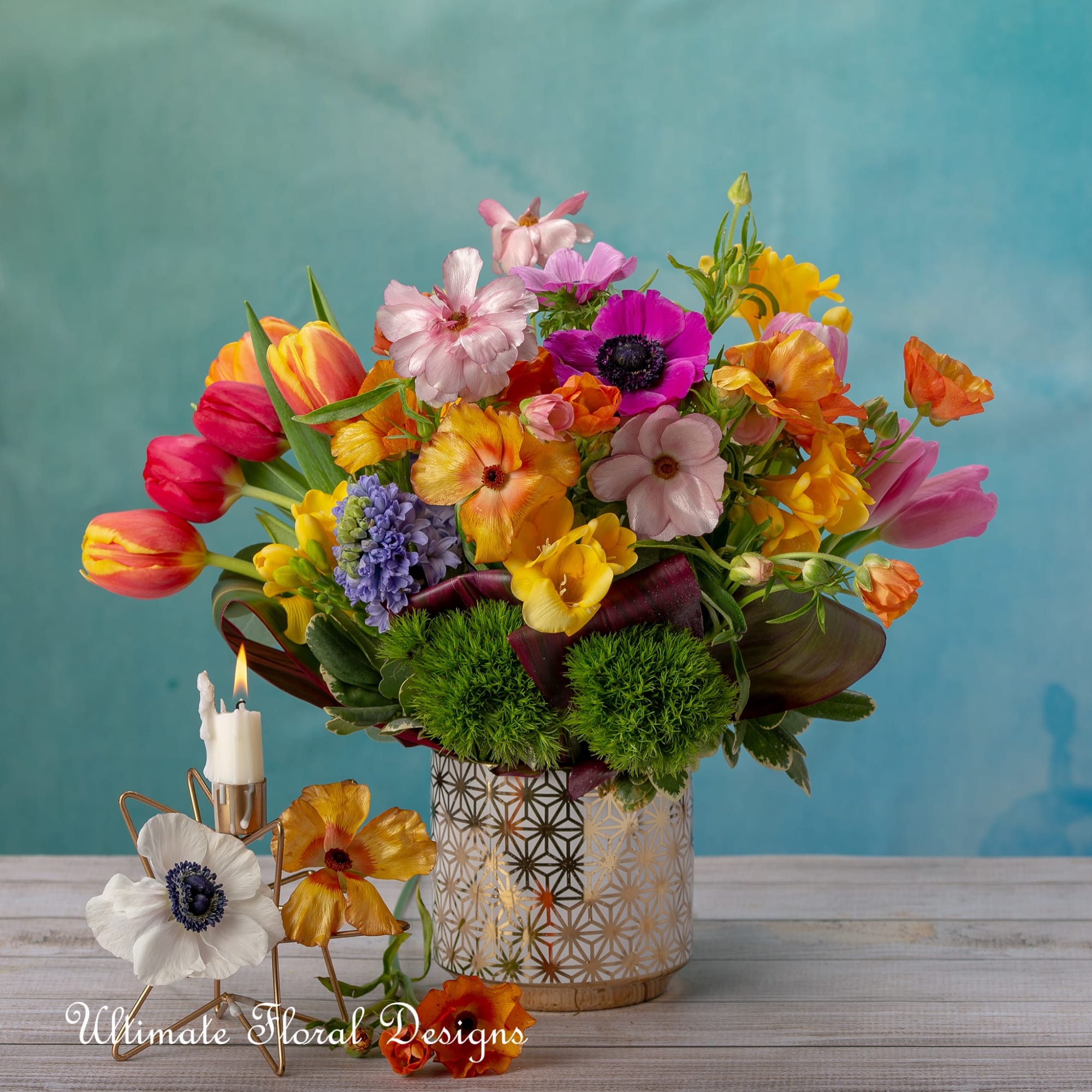 Colorful bouquet in a patterned vase with a lit candle beside it