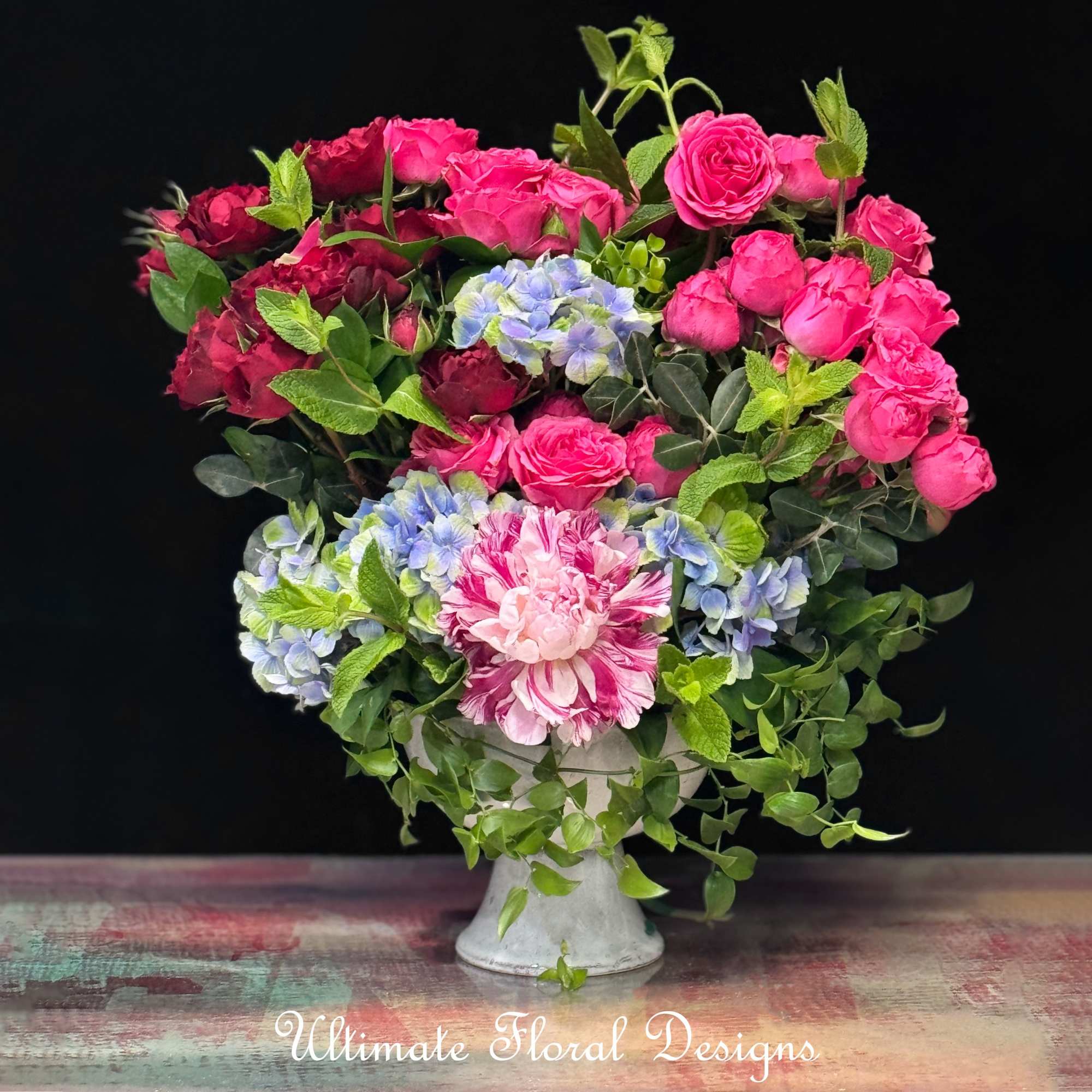 Pink and red roses with blue hydrangeas in a white vase