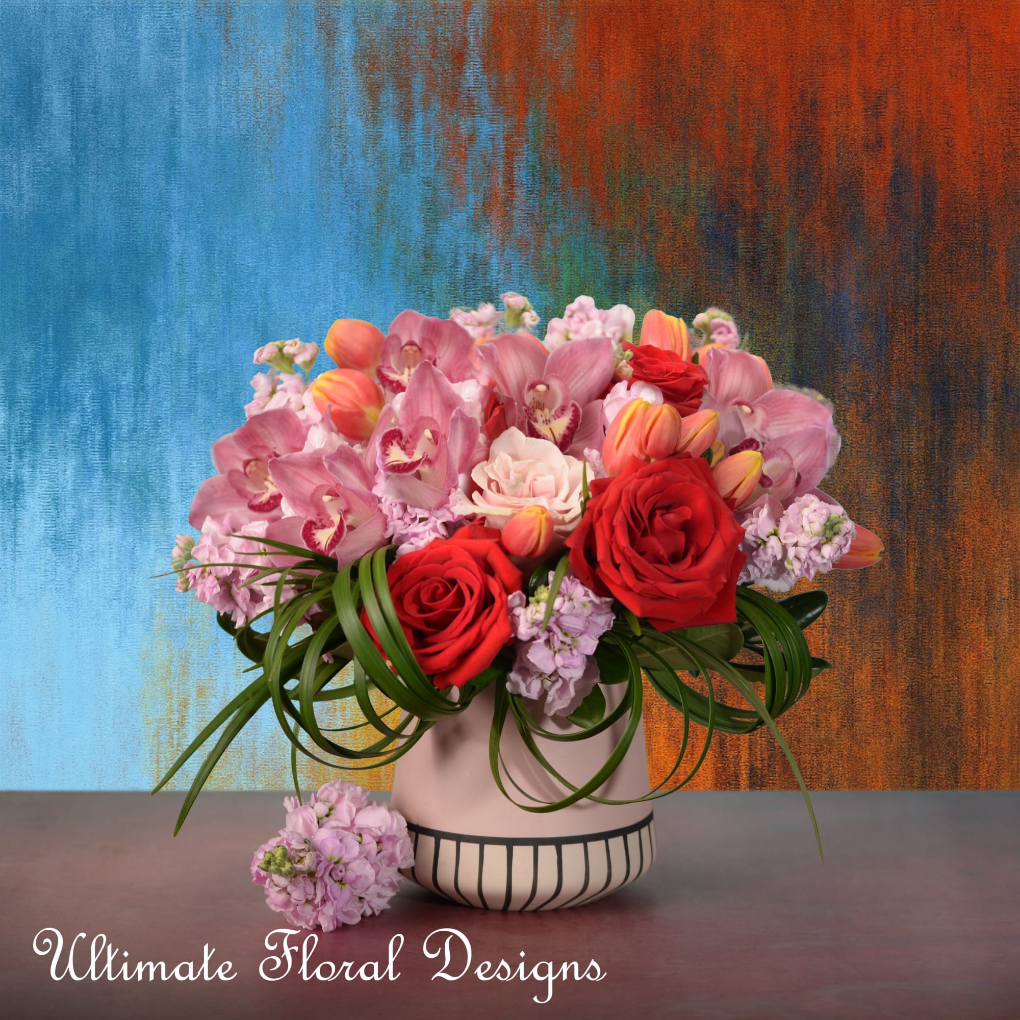 Pink orchids and red roses in a striped vase with trailing greenery