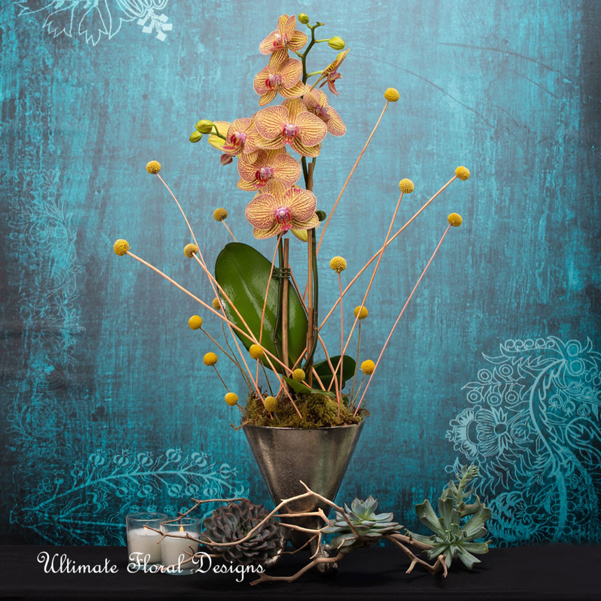 Orchid arrangement in a metal vase with succulents and candles