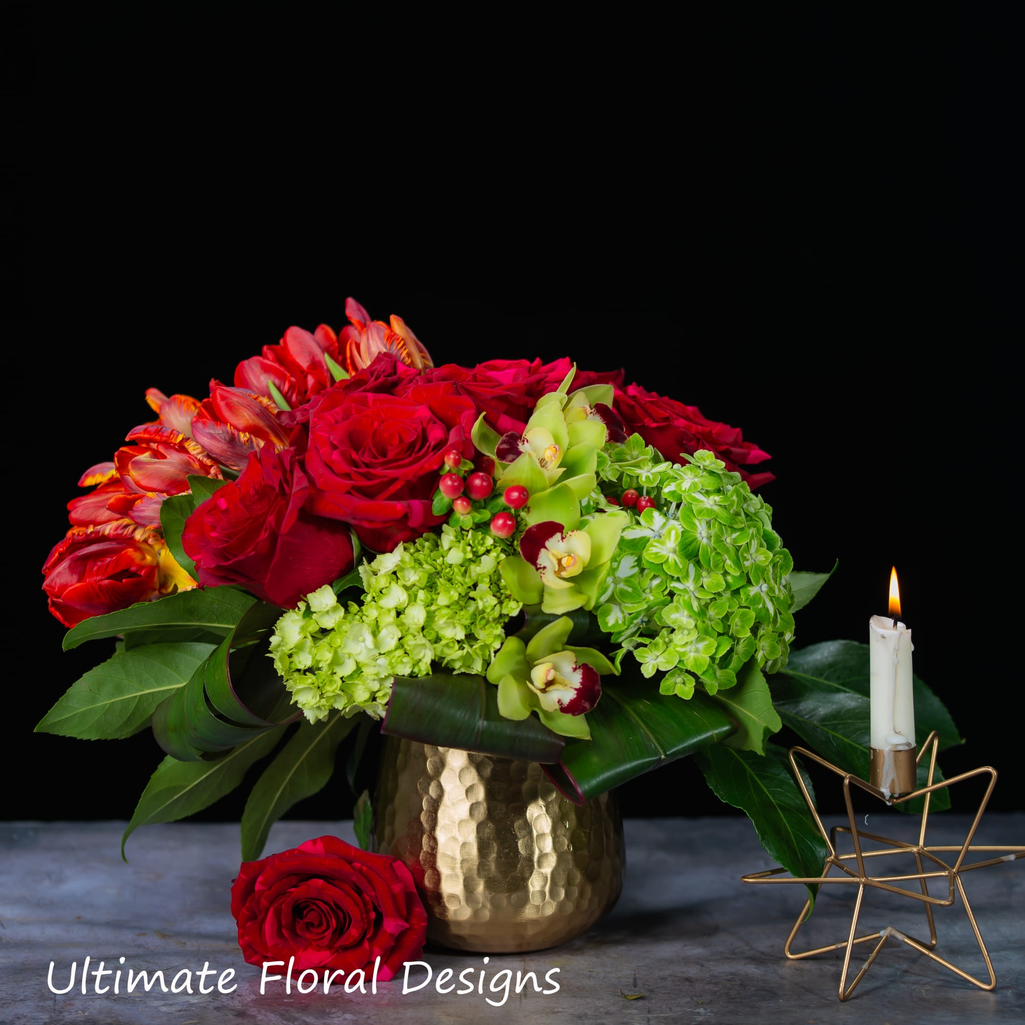 Red roses and green orchids in a gold vase beside a lit candle