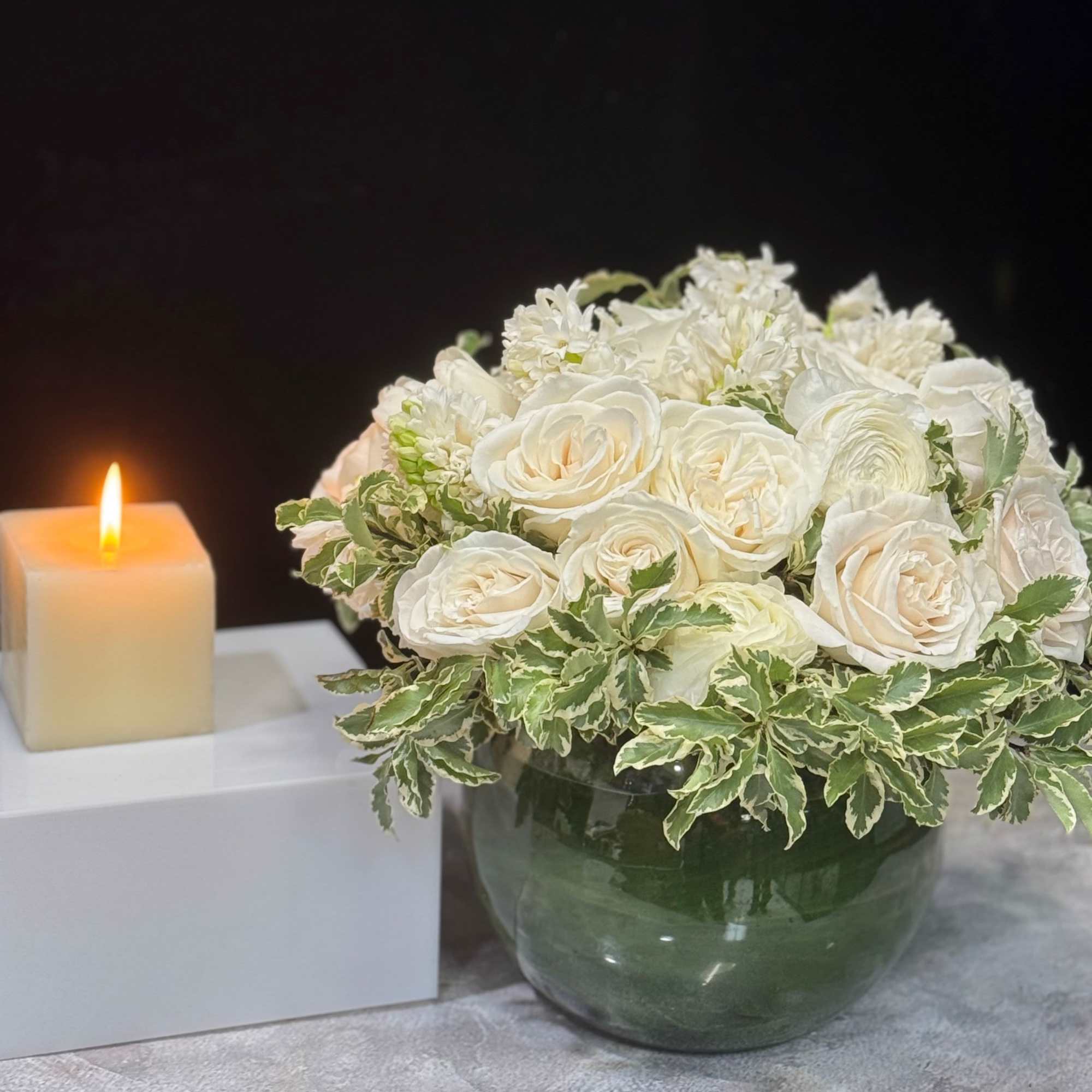 White rose bouquet in a glass vase beside a lit candle