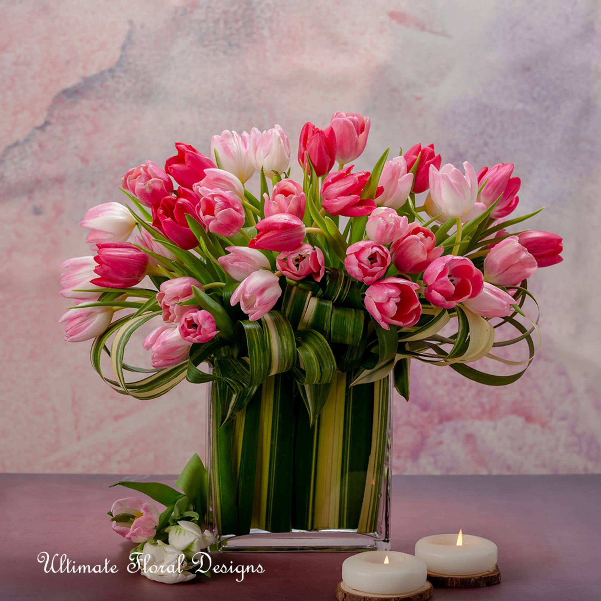 Pink and white tulips in a clear rectangular vase with candles nearby