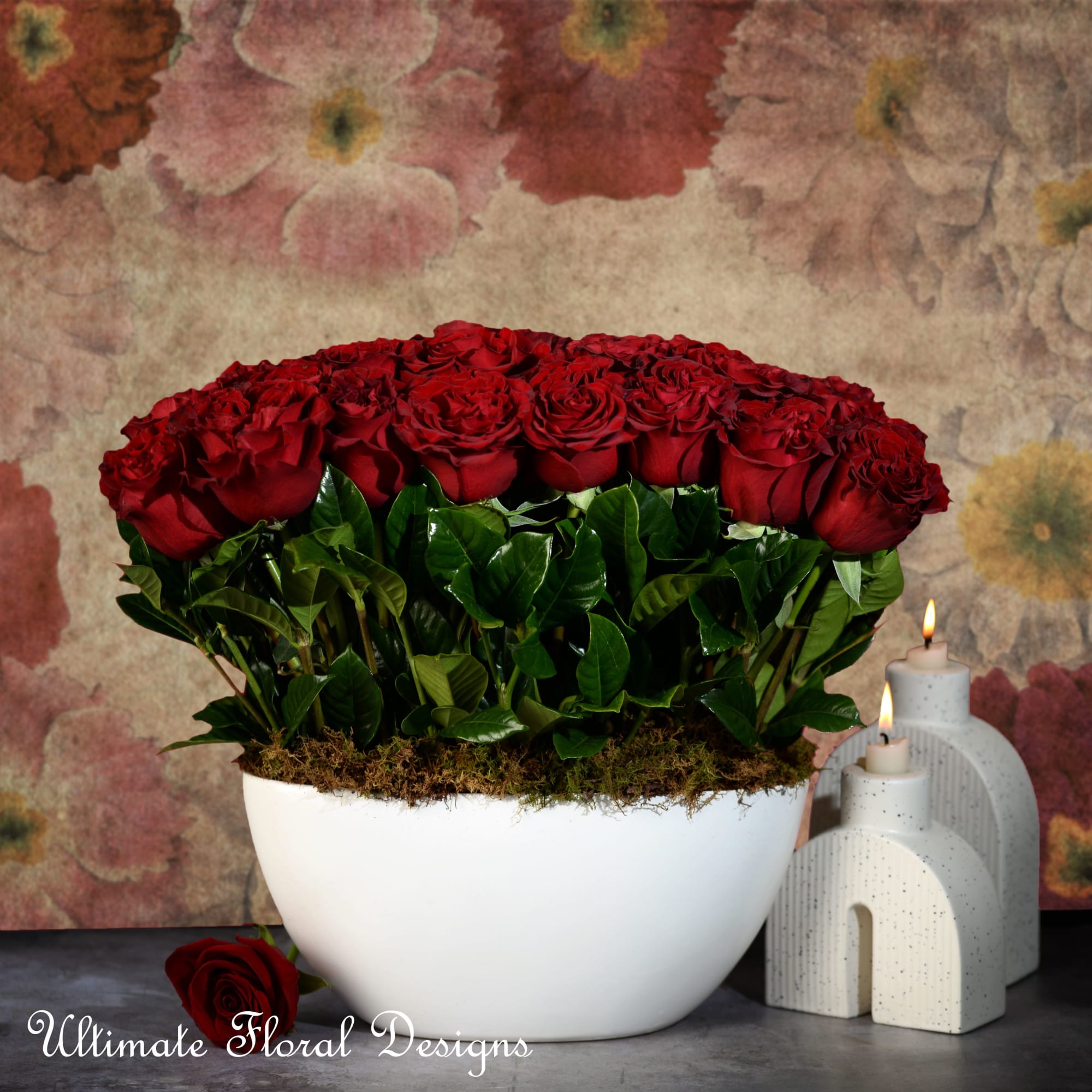 Red roses arranged in a white bowl with candles beside it