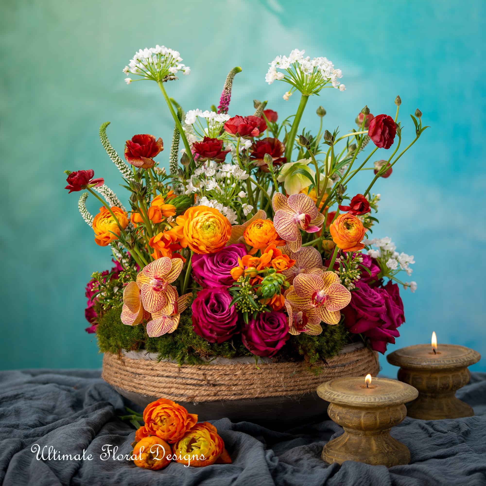 Colorful mixed flower arrangement in a low basket with lit candles nearby