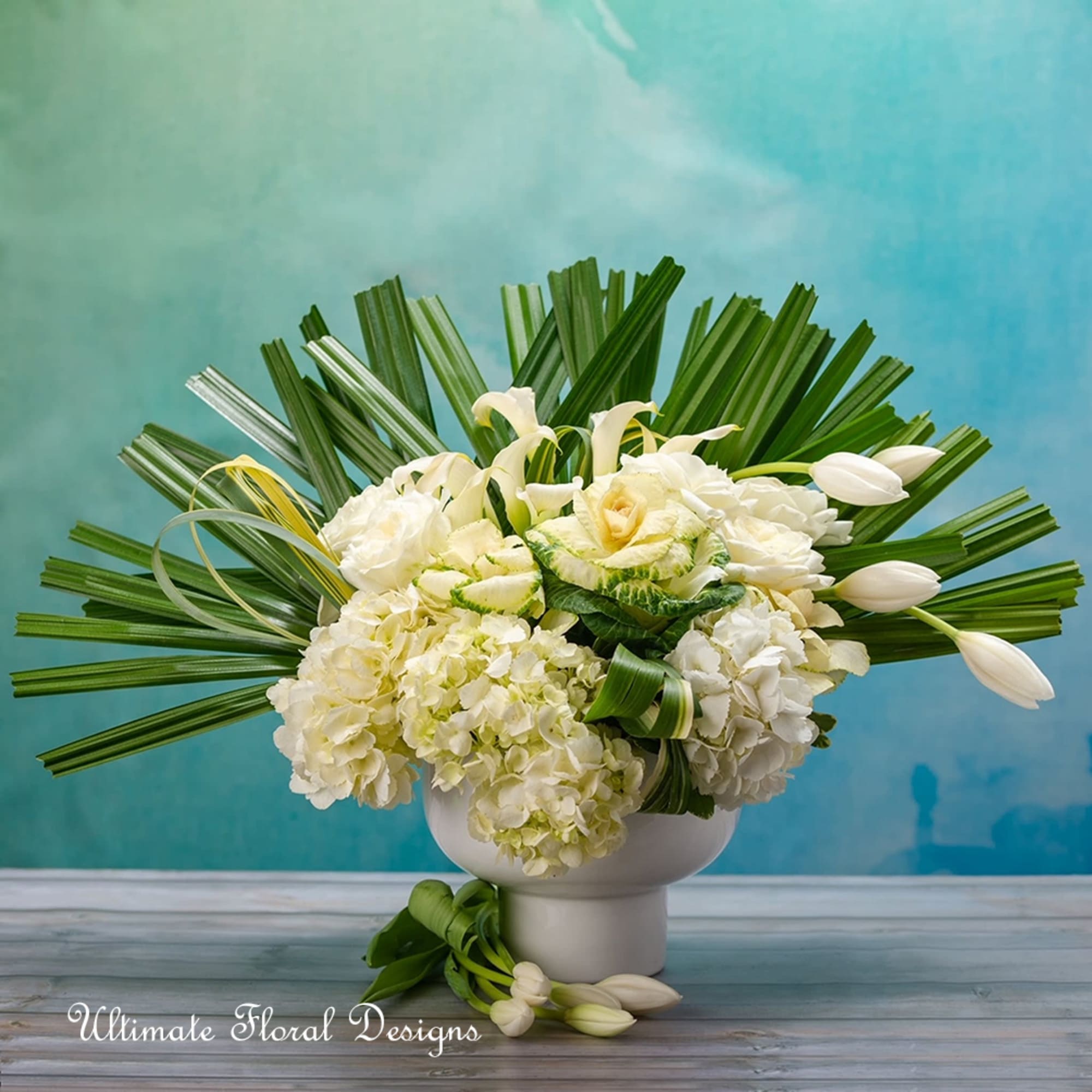 White floral arrangement in a white vase with fan-shaped palm leaves