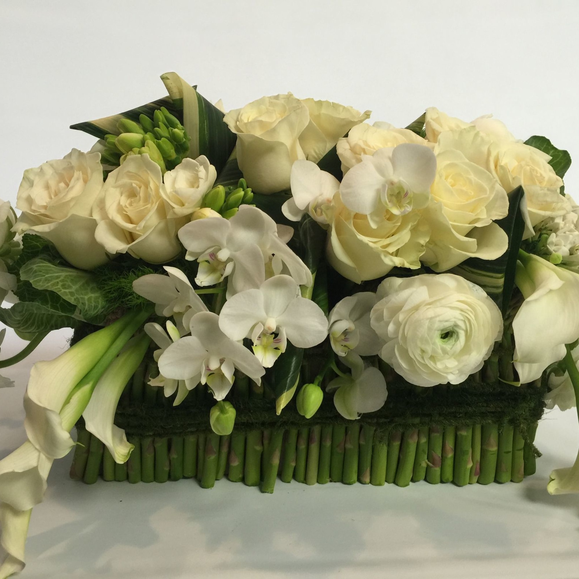 White floral arrangement with roses, orchids, calla lilies, and ranunculus in a low rectangular base