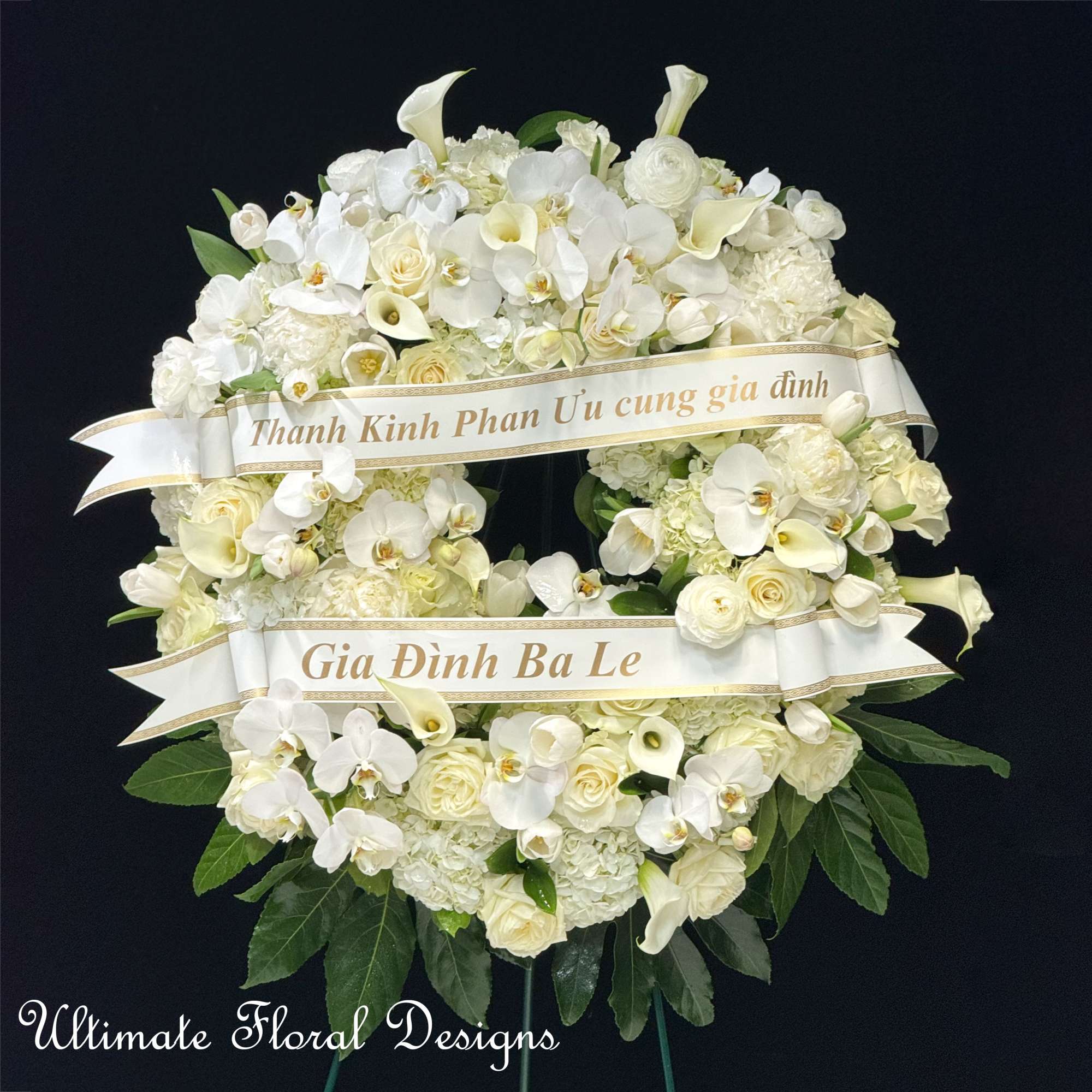 White funeral wreath with orchids, roses, and calla lilies on a black background