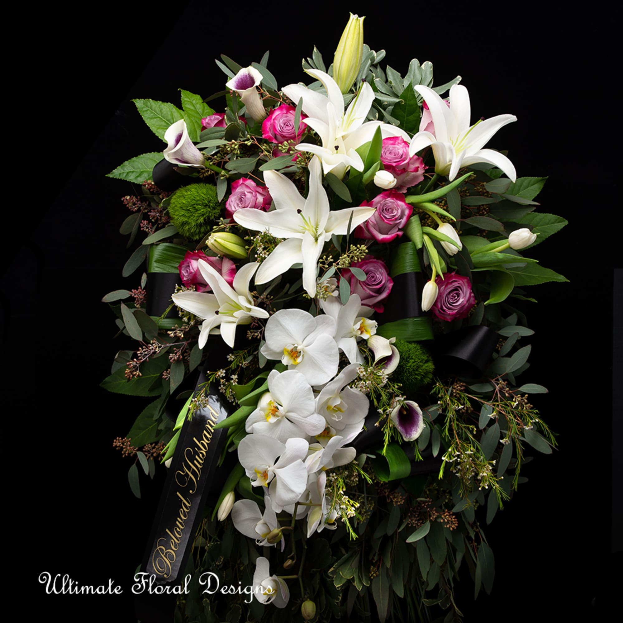Large funeral spray with white lilies, orchids, and pink roses on a black ribbon