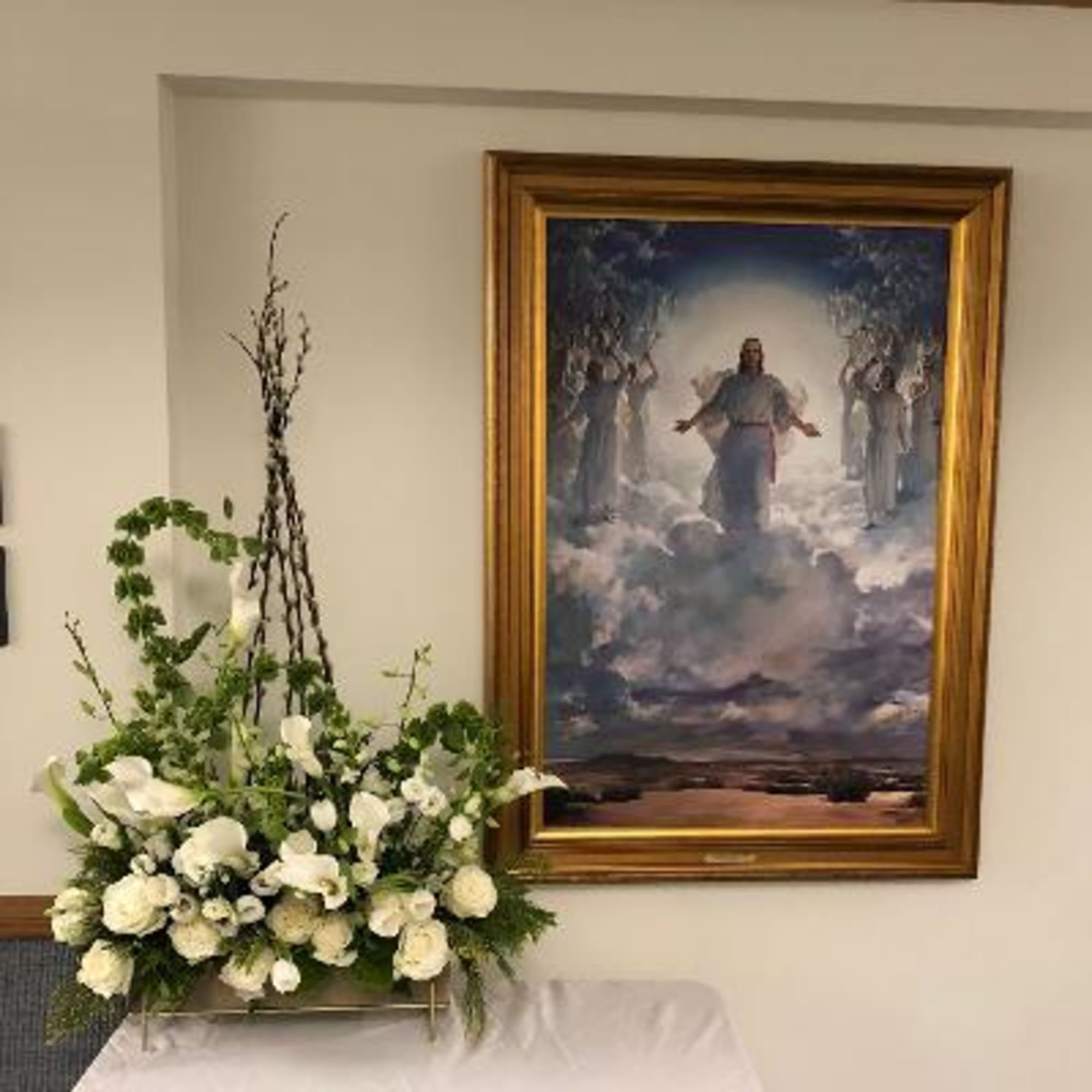 White floral arrangement on a stand beside a framed painting
