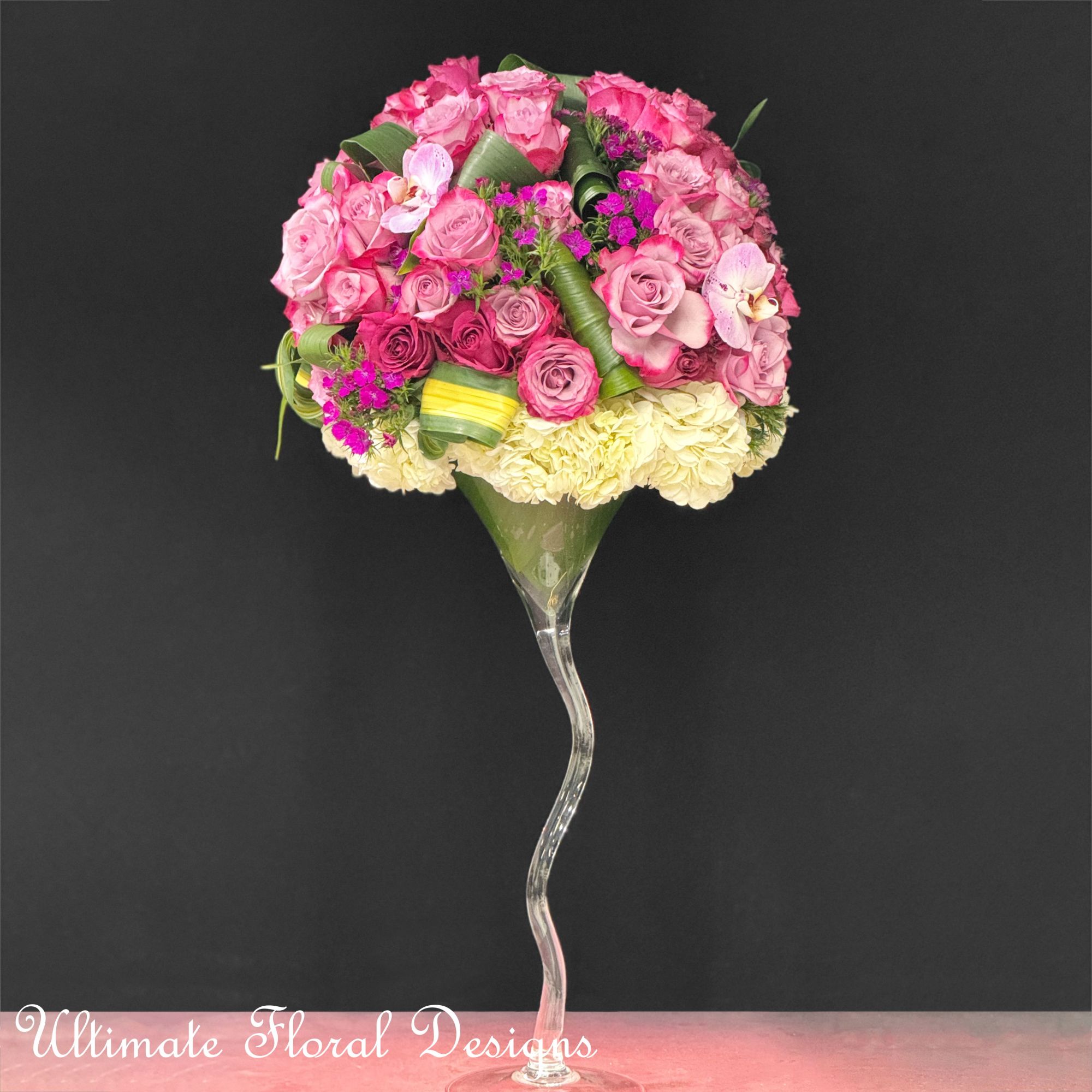 Pink rose bouquet in a tall clear glass vase with cream flowers at the base