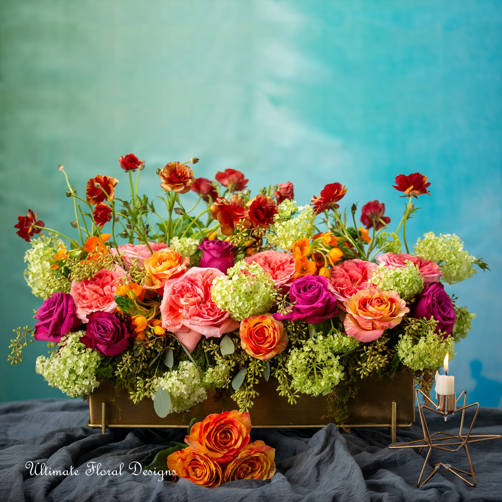 Colorful rose arrangement in a rectangular container with a candle holder beside it