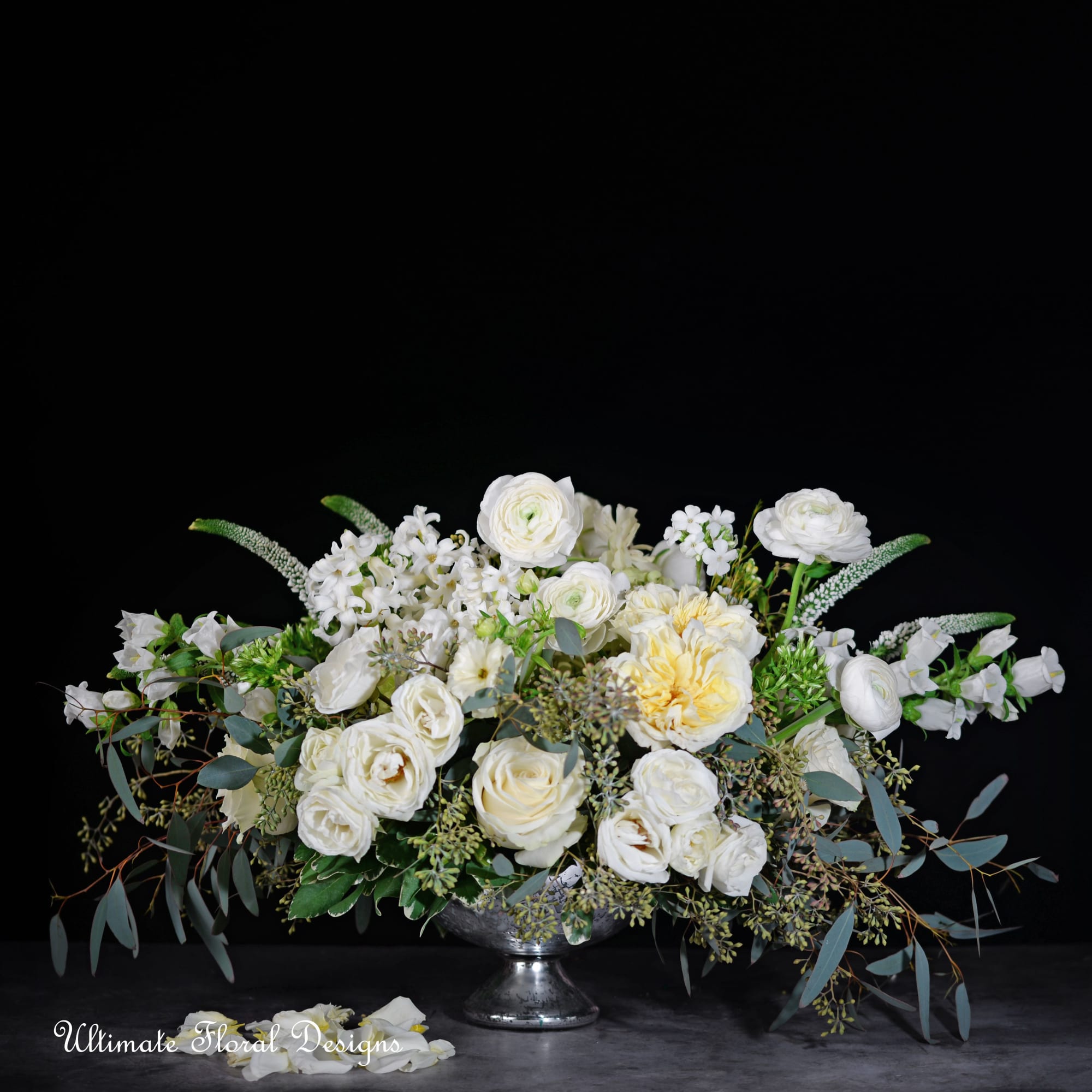 White floral arrangement in a silver pedestal bowl with trailing greenery